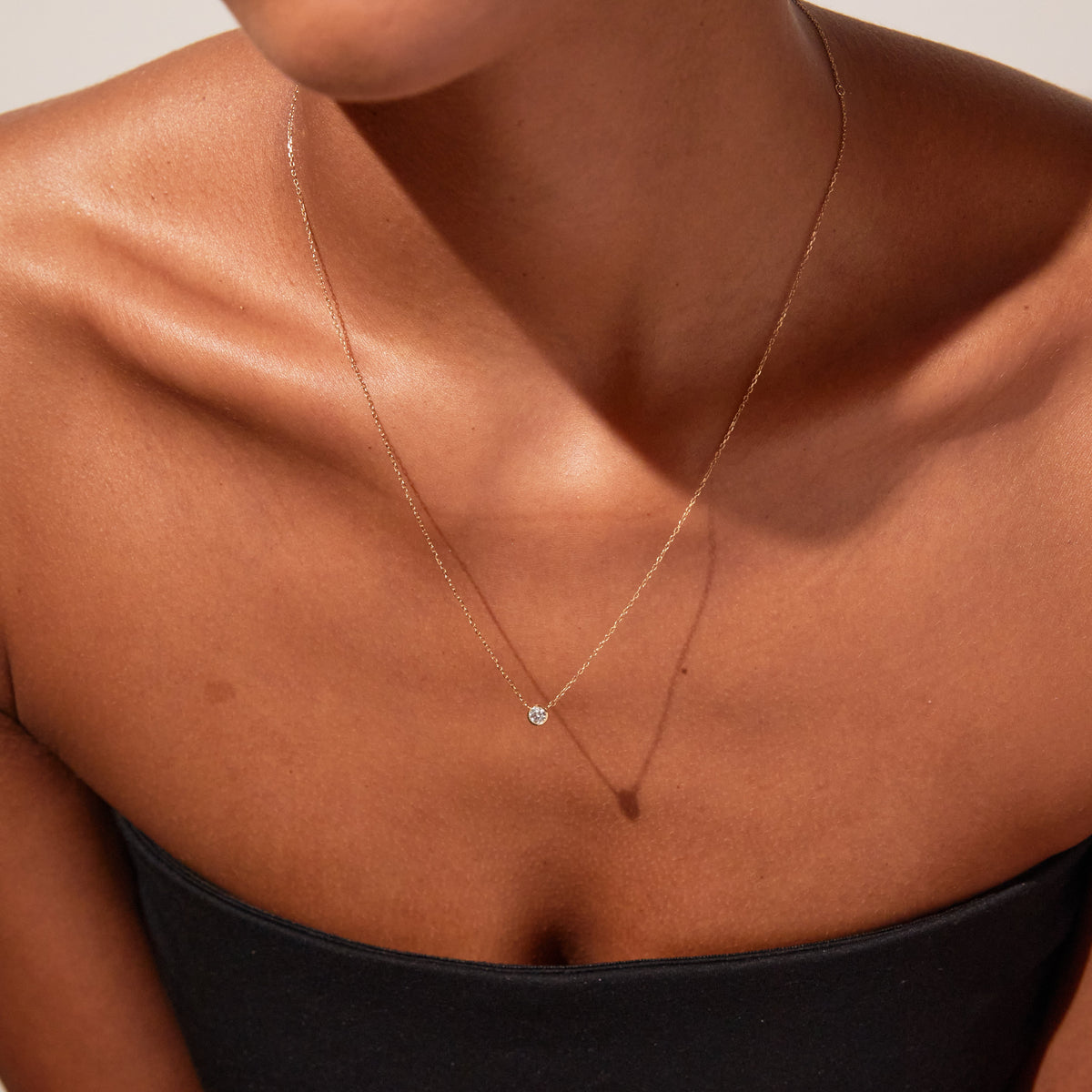Close up of woman wearing diamond bezel necklace and black tube top