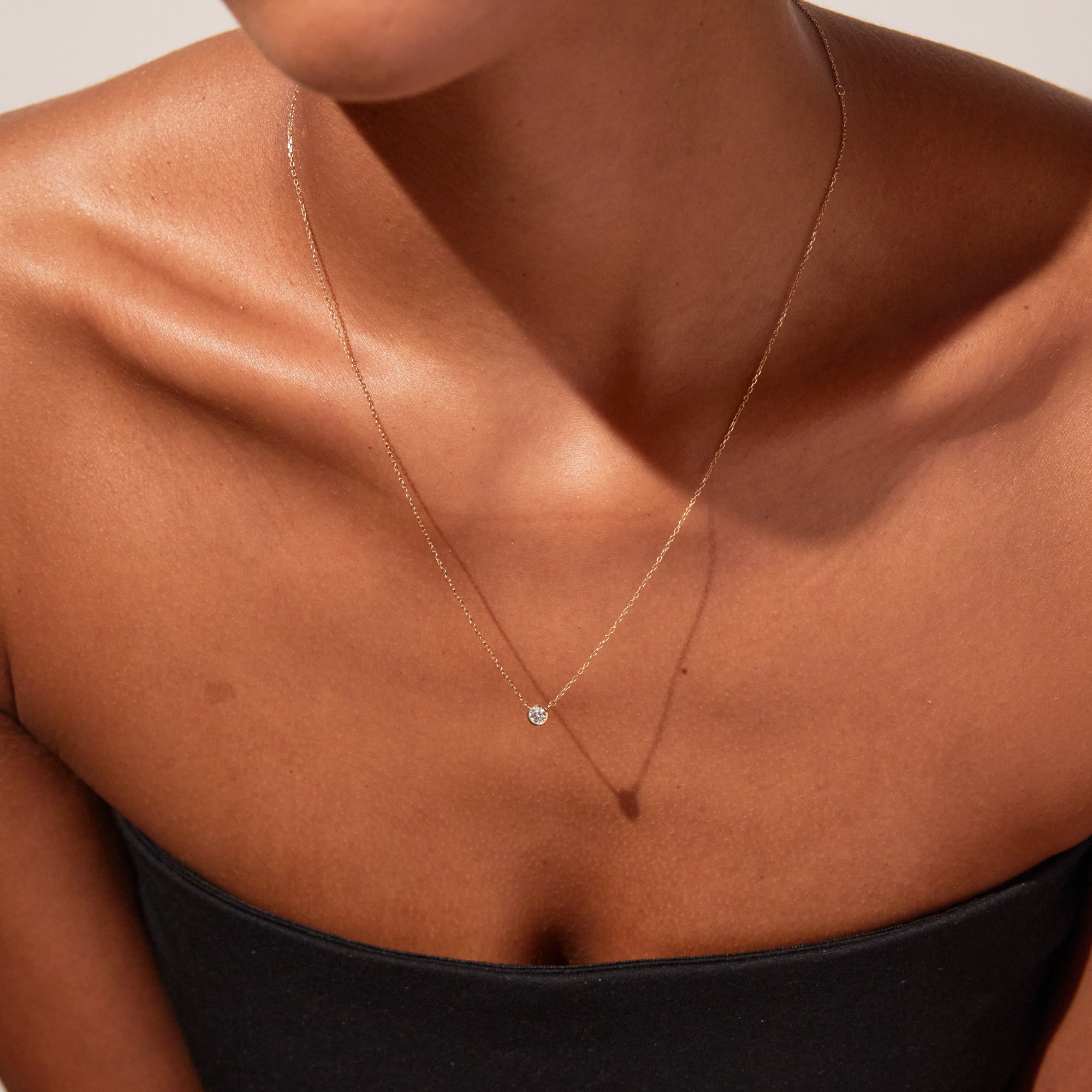 Close up of woman wearing diamond bezel necklace and black tube top