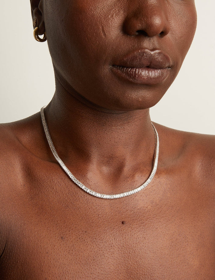 Person wearing a silver necklace on a neutral background
