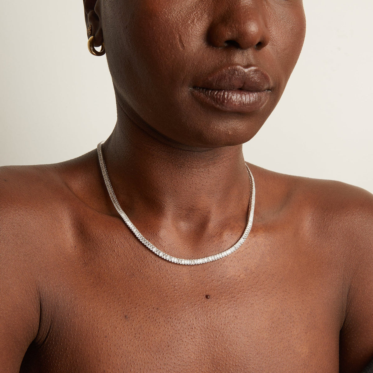 Person wearing a silver necklace on a neutral background