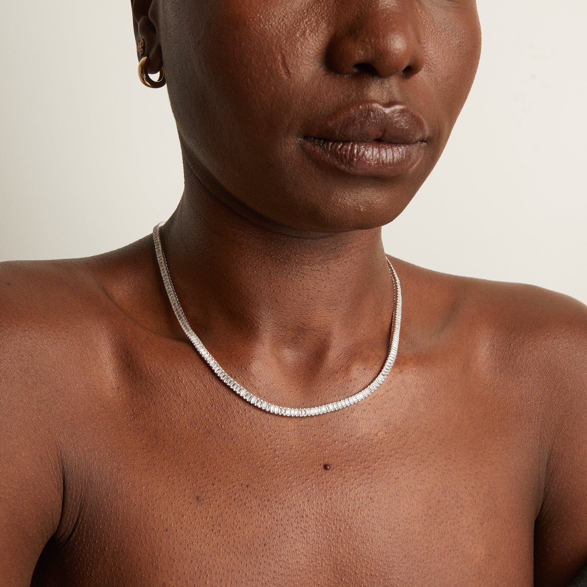 Person wearing a silver necklace on a neutral background
