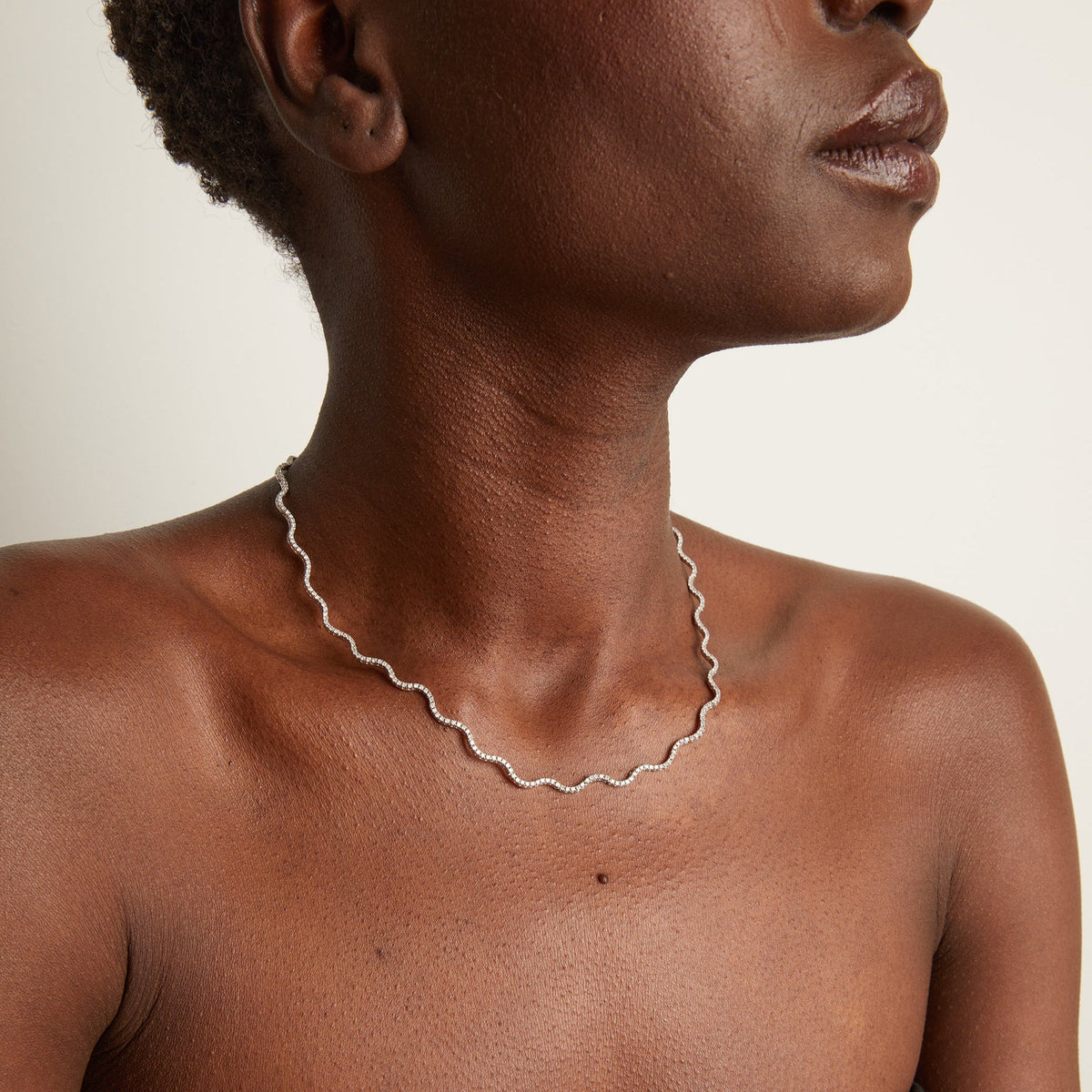 Model. Woman wearing wavy tennis necklace on neutral background