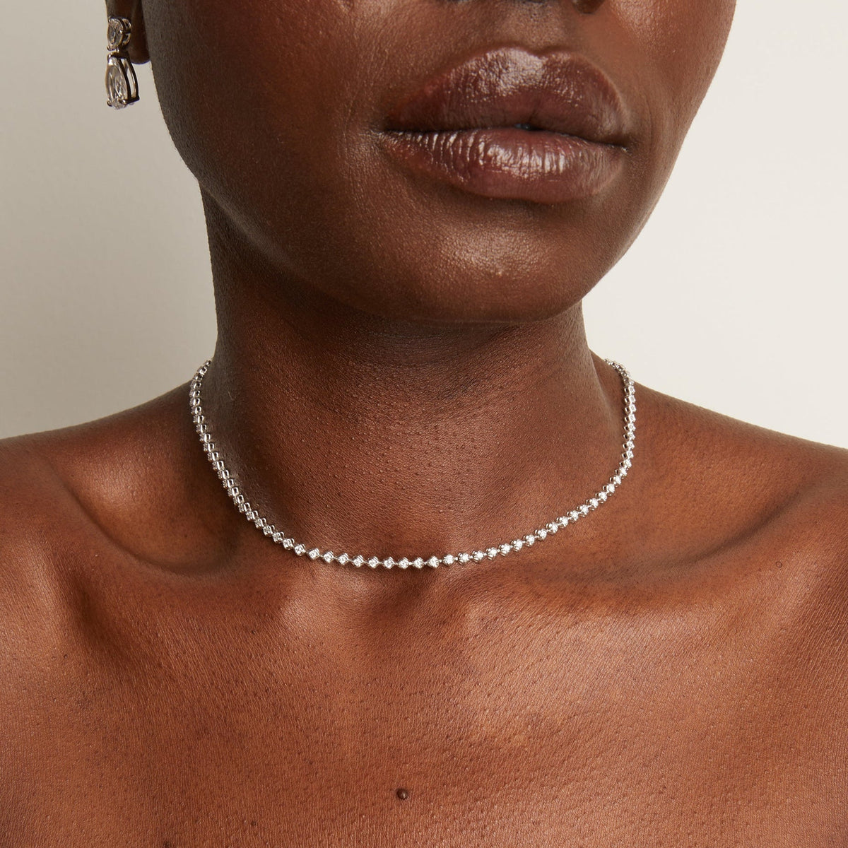 Model. Close-up of a person wearing a silver necklace with a neutral background
