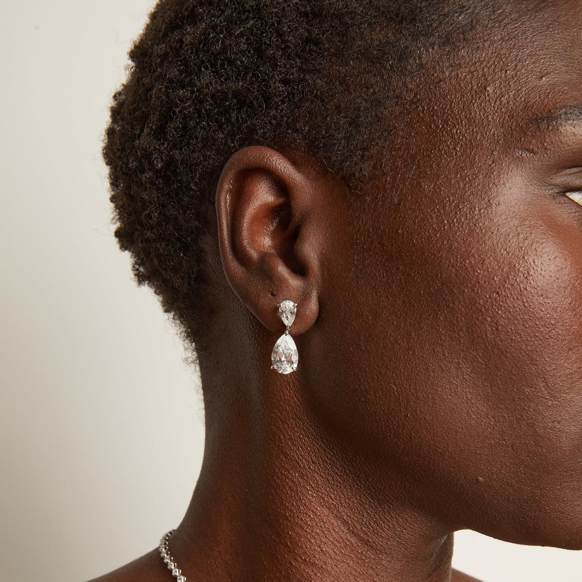 Model. Close-up of a person wearing a necklace and earrings with a neutral background