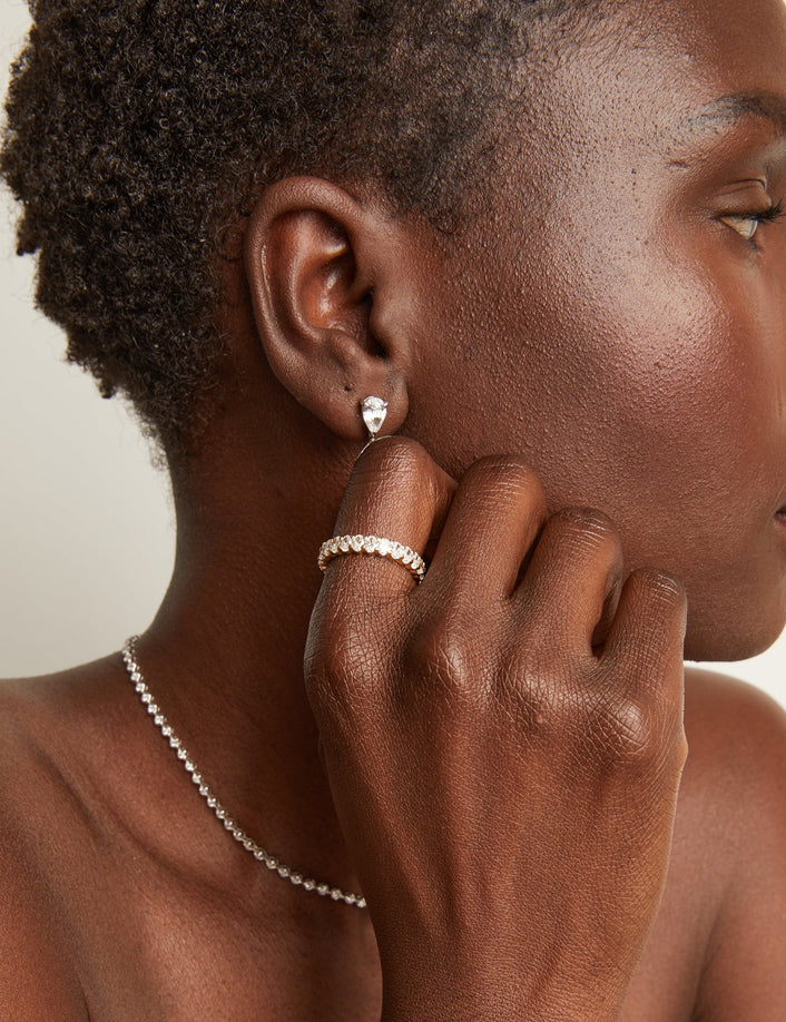 Woman wearing an eternity ring and drop earrings on a neutral background
