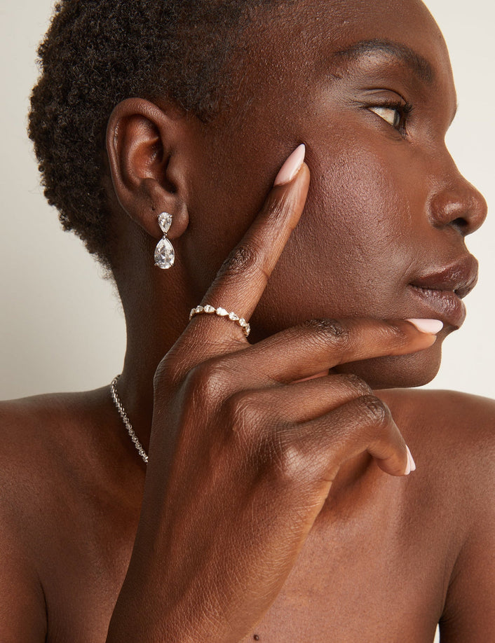 Woman wearing earrings and a ring, touching her face against a neutral background