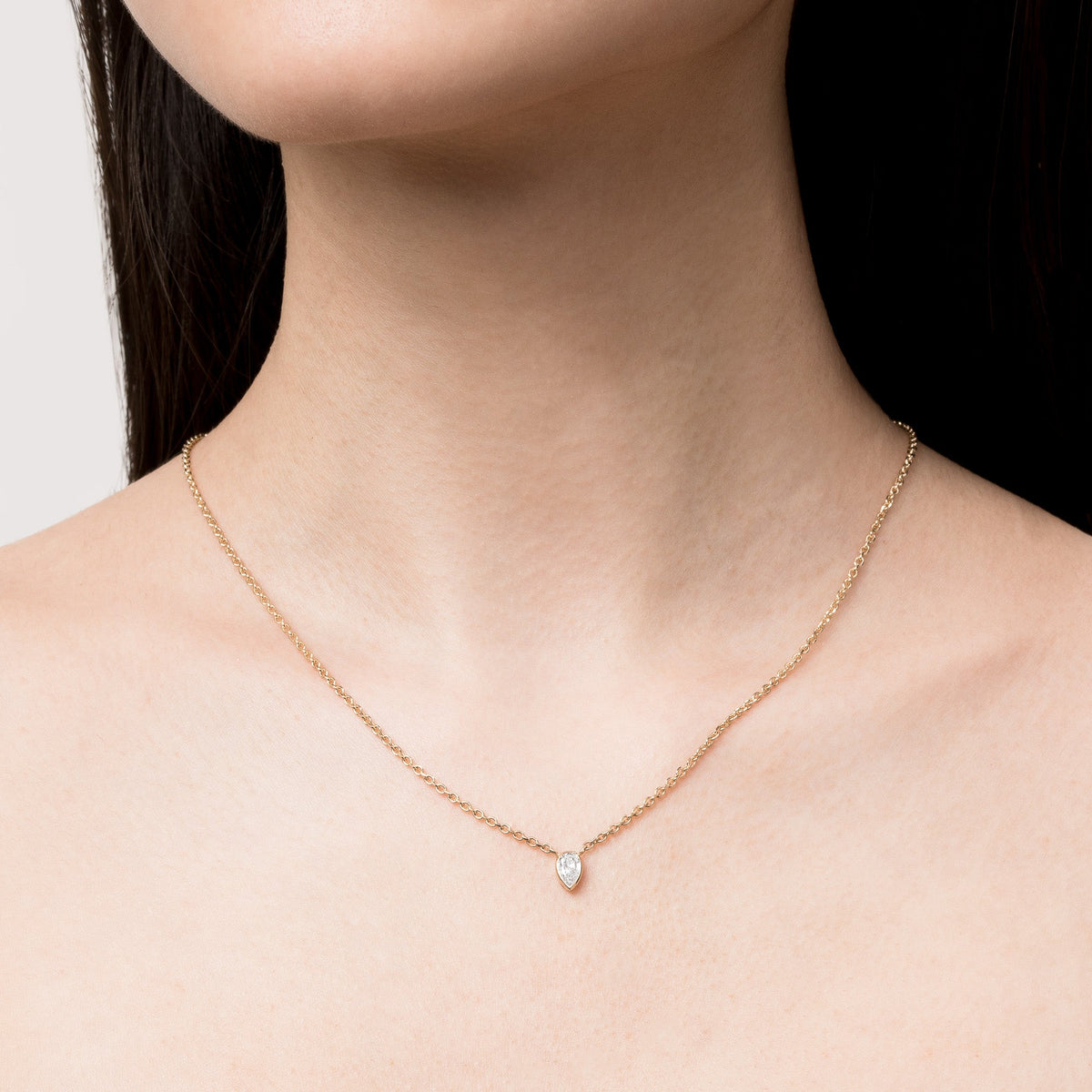 Model Close-up of a woman's neck and collarbone wearing a delicate gold chain necklace with a single pear-shaped, bezel-set diamond pendant.