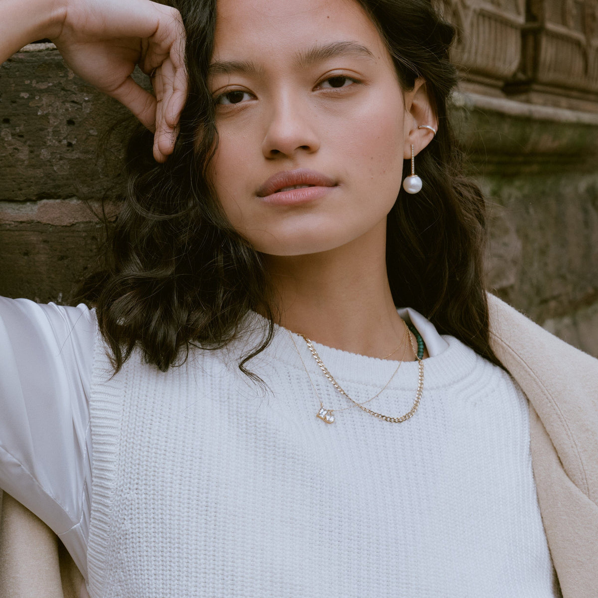 Lifestyle Model. Woman wearing stacked necklaces and pearl earrings outside.