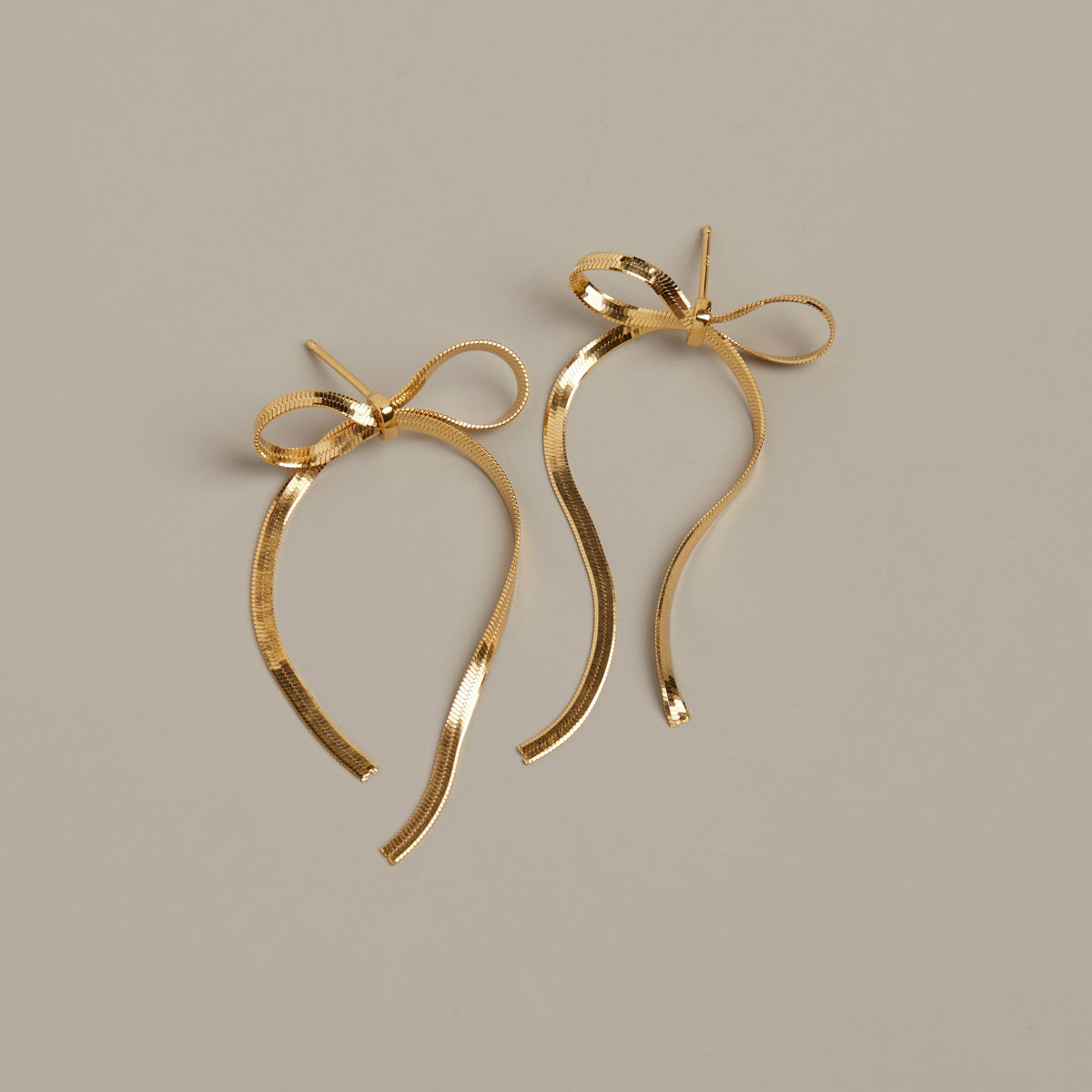 Flatlay Model. Gold bow earring on beige background
