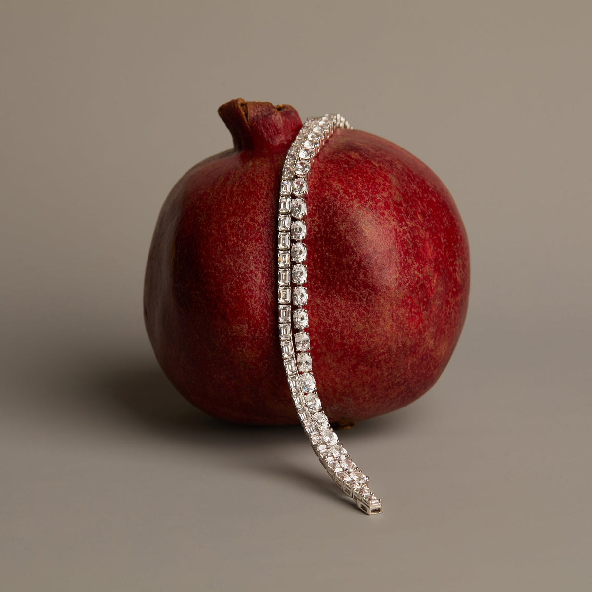 Flatlay Model. Silver bracelet with clear stones on a red pomegranate against a gray background