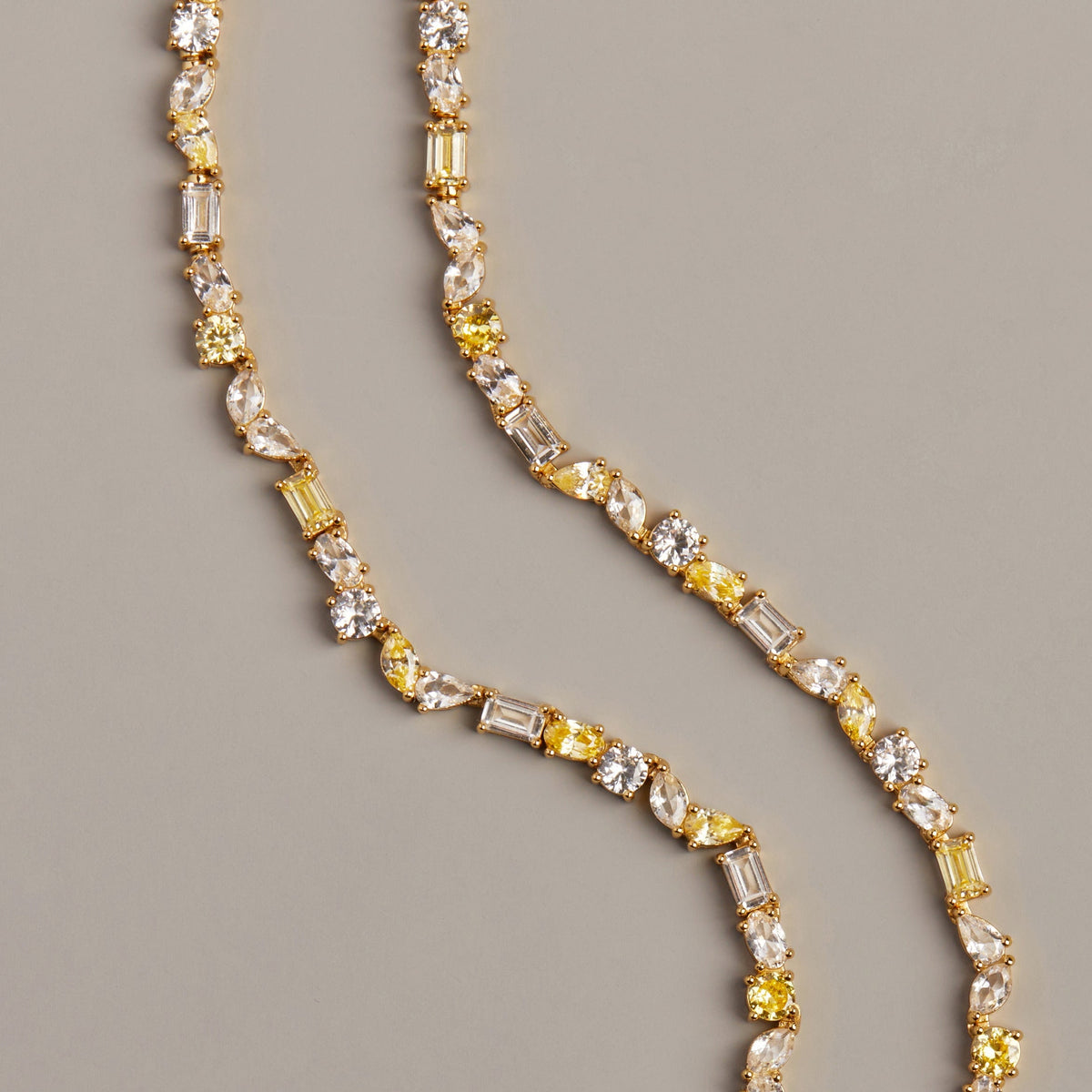Model. Gold necklace with yellow and clear gemstones on a gray background