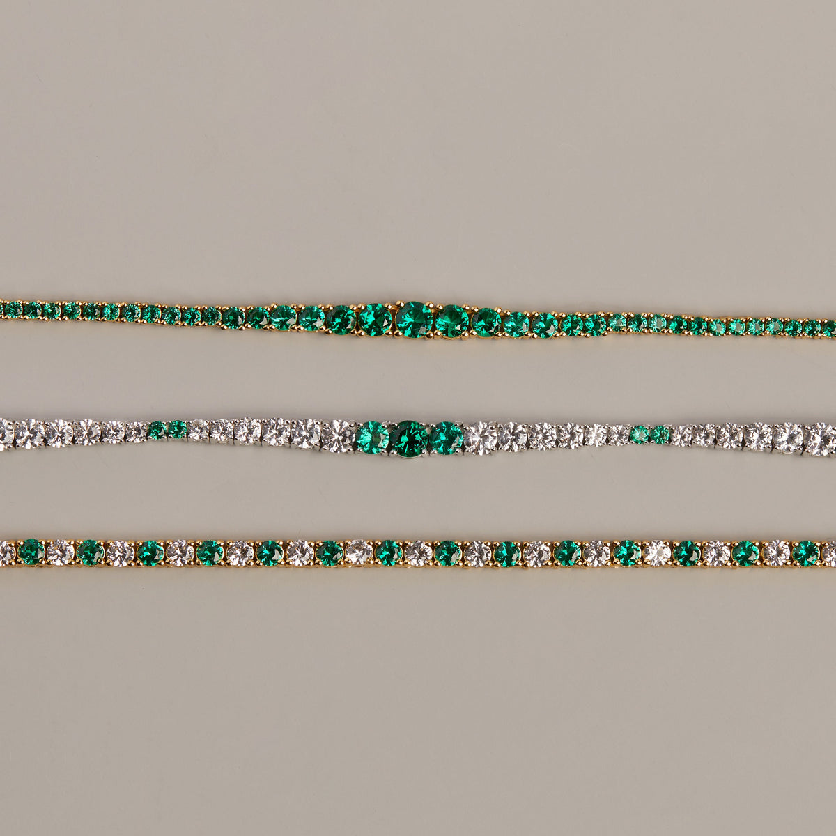 Model. Two gold bracelets with green gemstones on a beige background