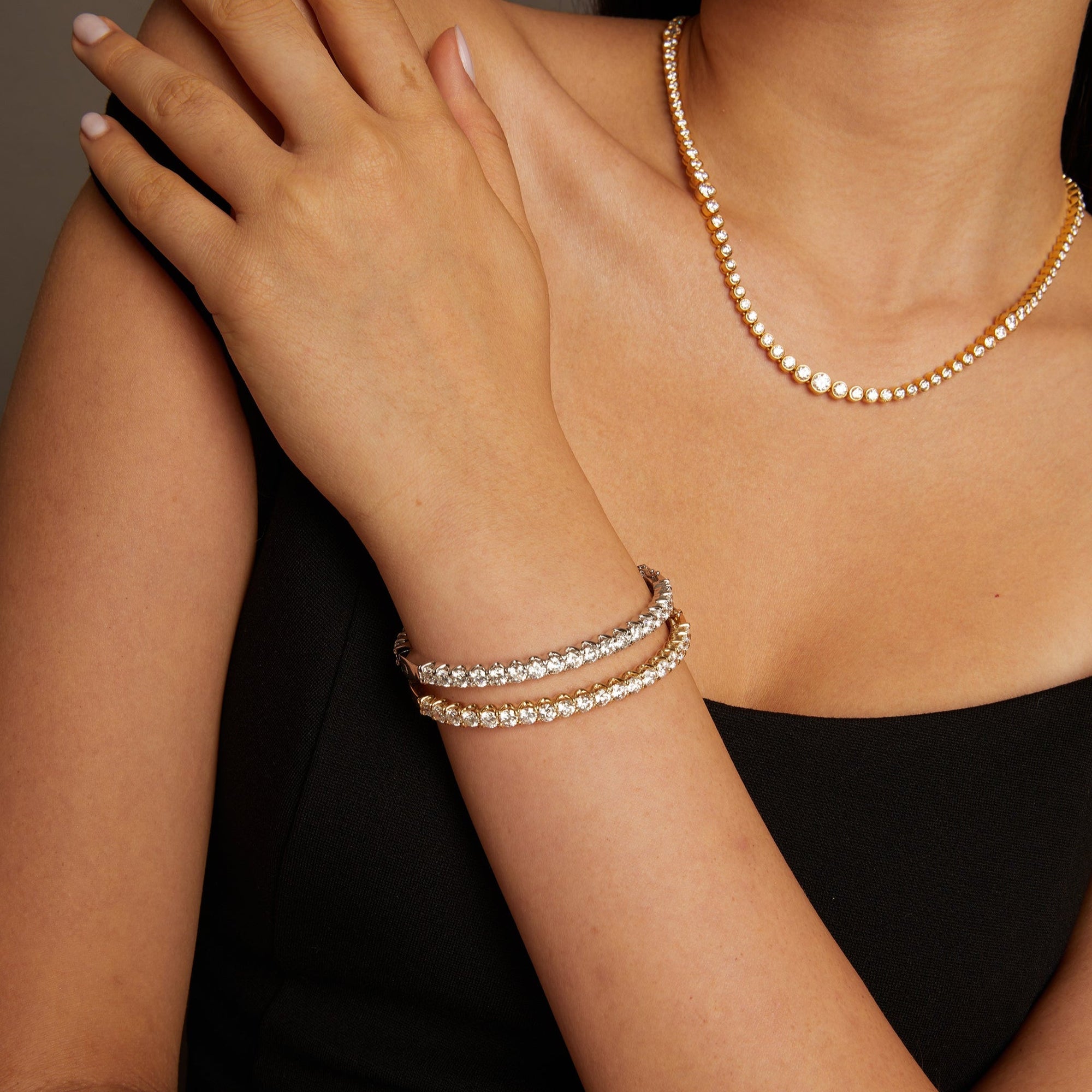 Model. Close-up of a person wearing a gold necklace and pearl bracelets on a neutral background