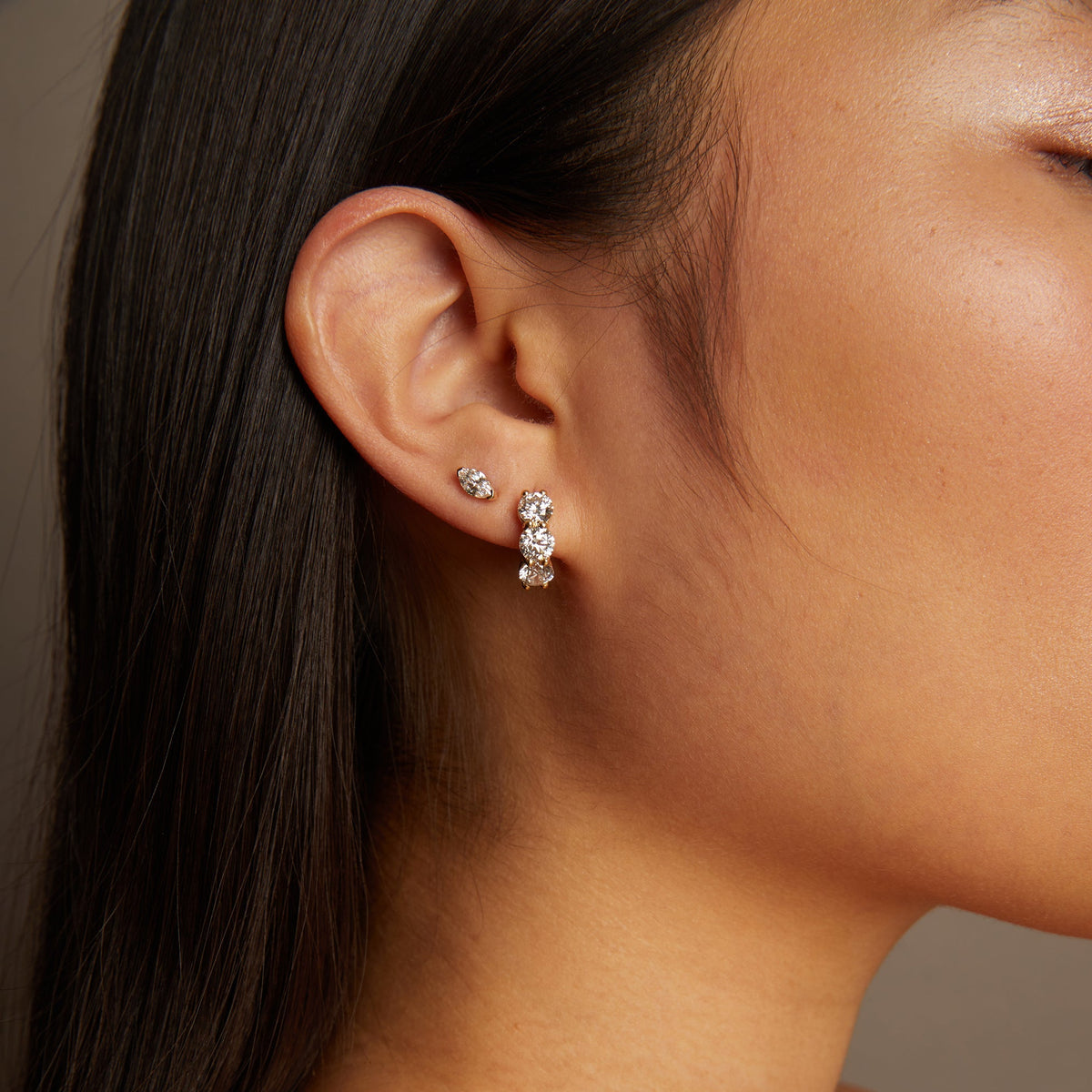 Model. Close-up of a person wearing a gold necklace and diamond earrings against a neutral background