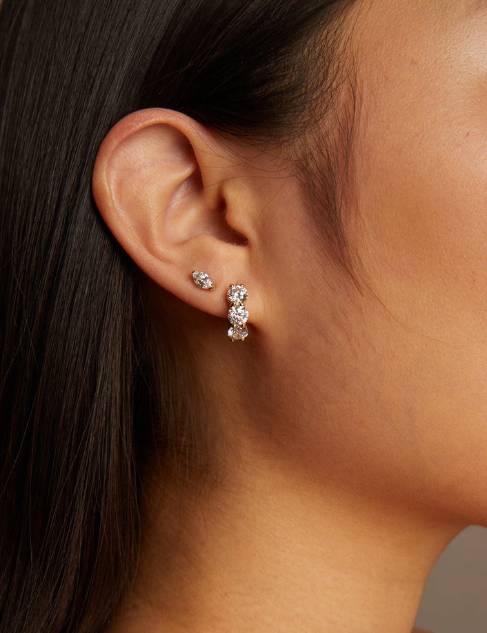 Close-up of a person wearing diamond hoop earrings with a neutral background