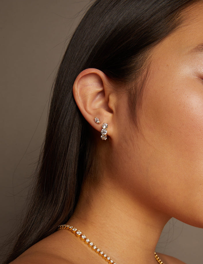 Model. Close-up of a woman wearing a gold necklace and diamond earrings against a neutral background