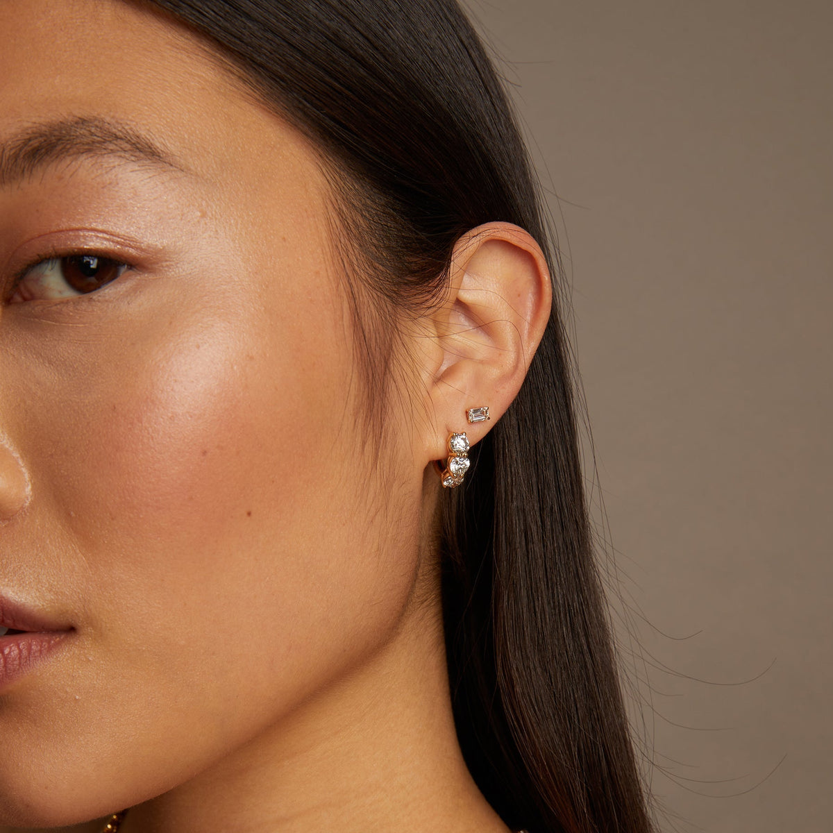 Model. Close-up of a woman wearing gold necklace and earrings against a neutral background