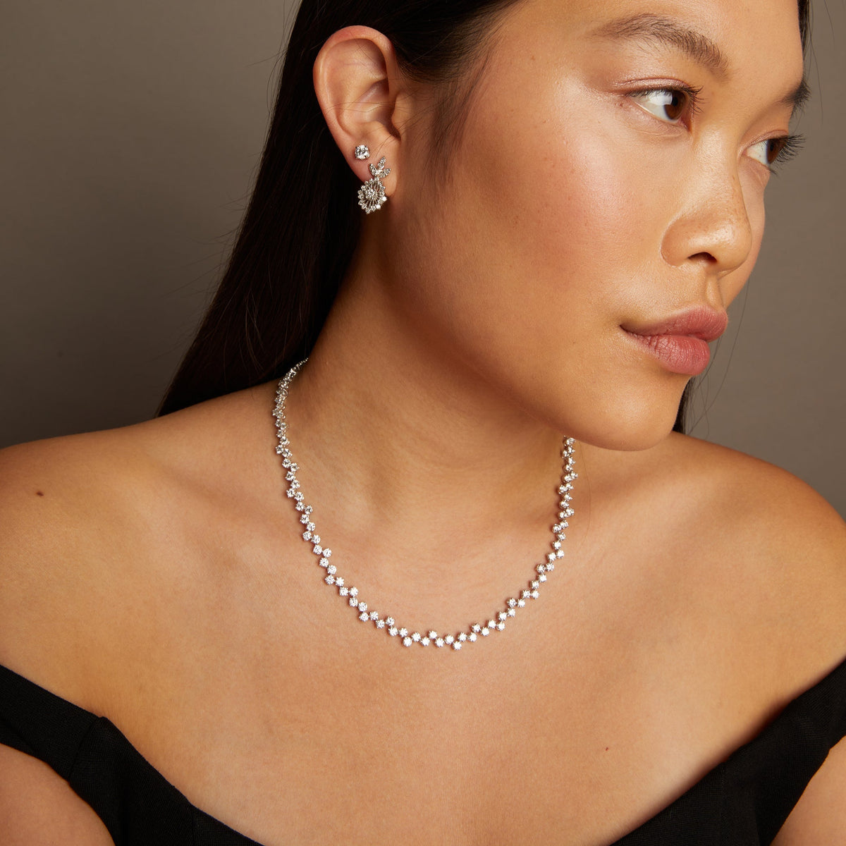 Model. Woman wearing a necklace and earrings against a neutral background