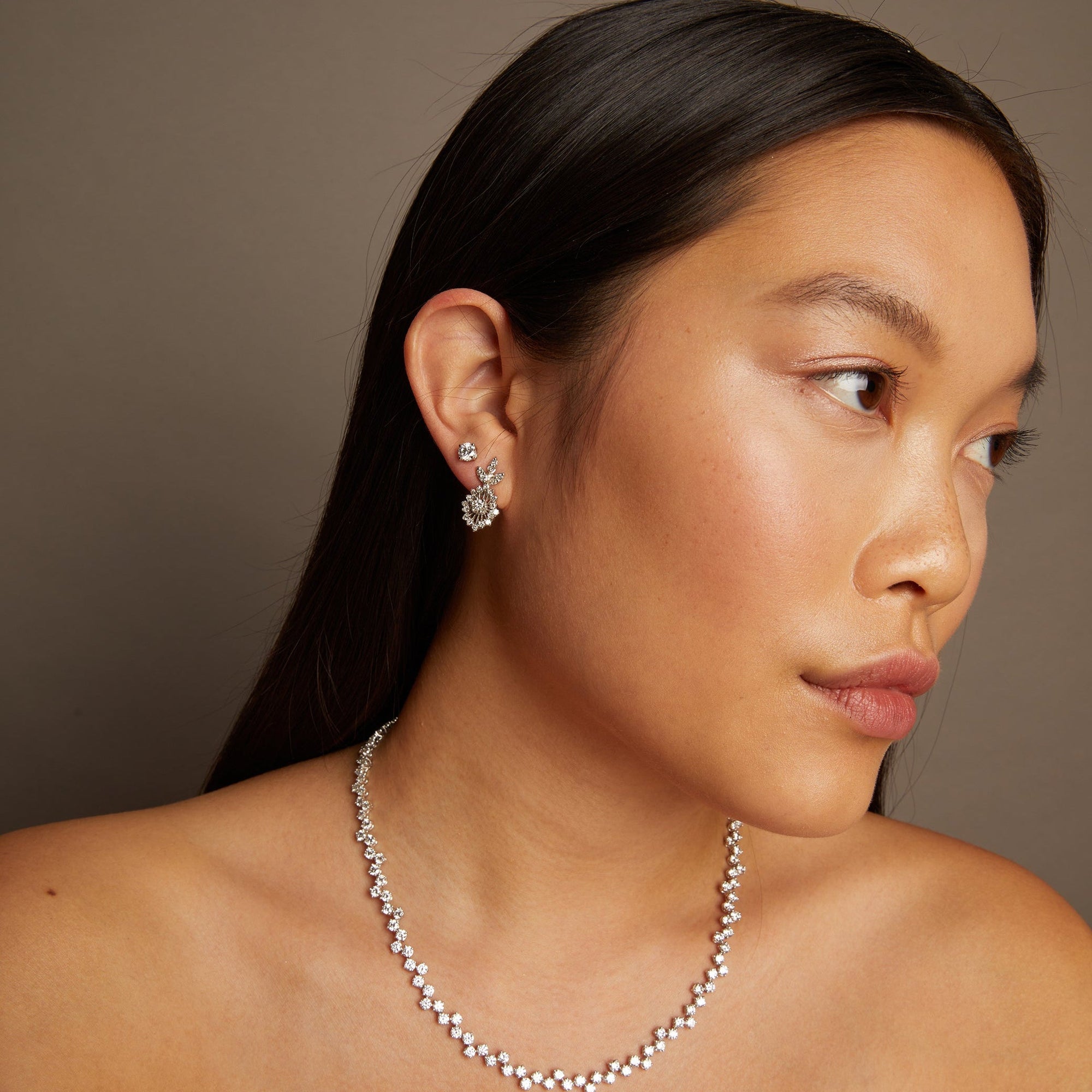 Model. Woman wearing a necklace and earrings against a neutral background