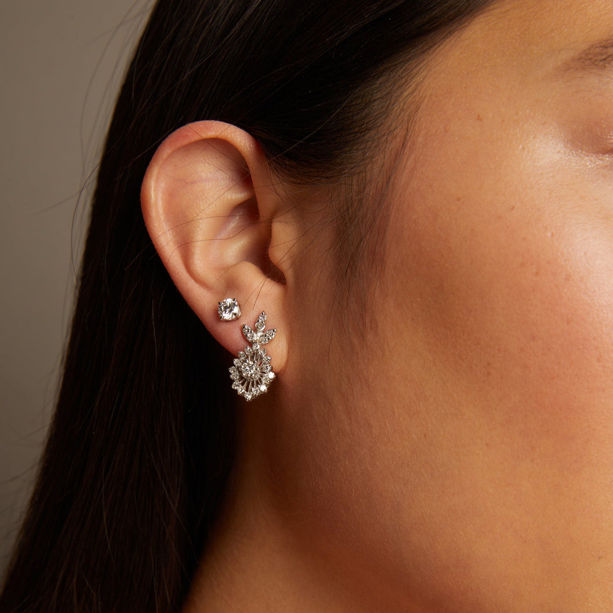 Model. Close-up of a person wearing elegant earrings and a necklace against a neutral background