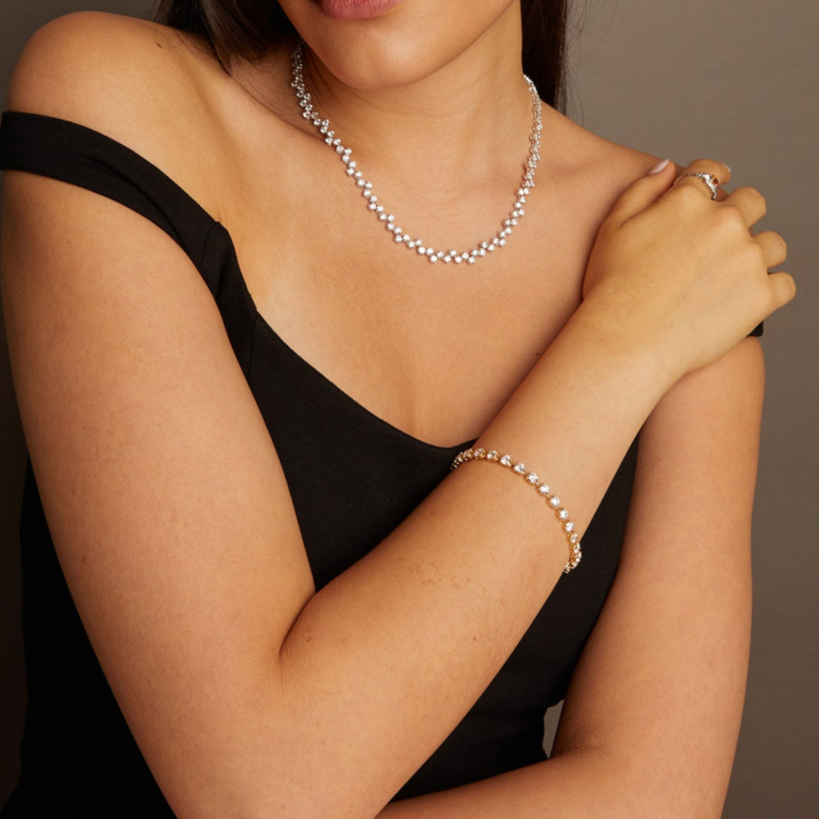 Model. Woman wearing a black dress and jewelry against a neutral background