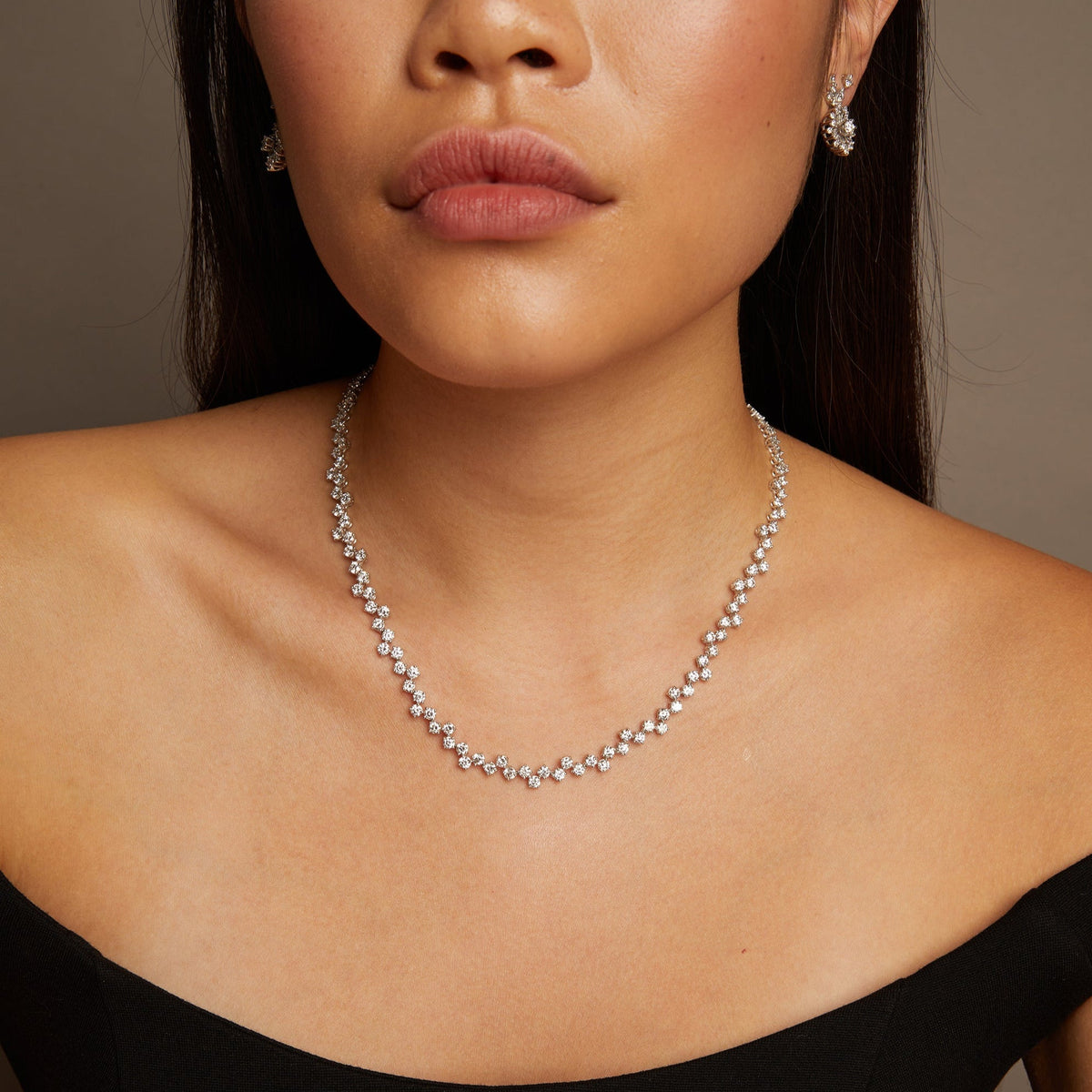 Model. Close-up of a woman wearing a silver necklace and earrings against a neutral background