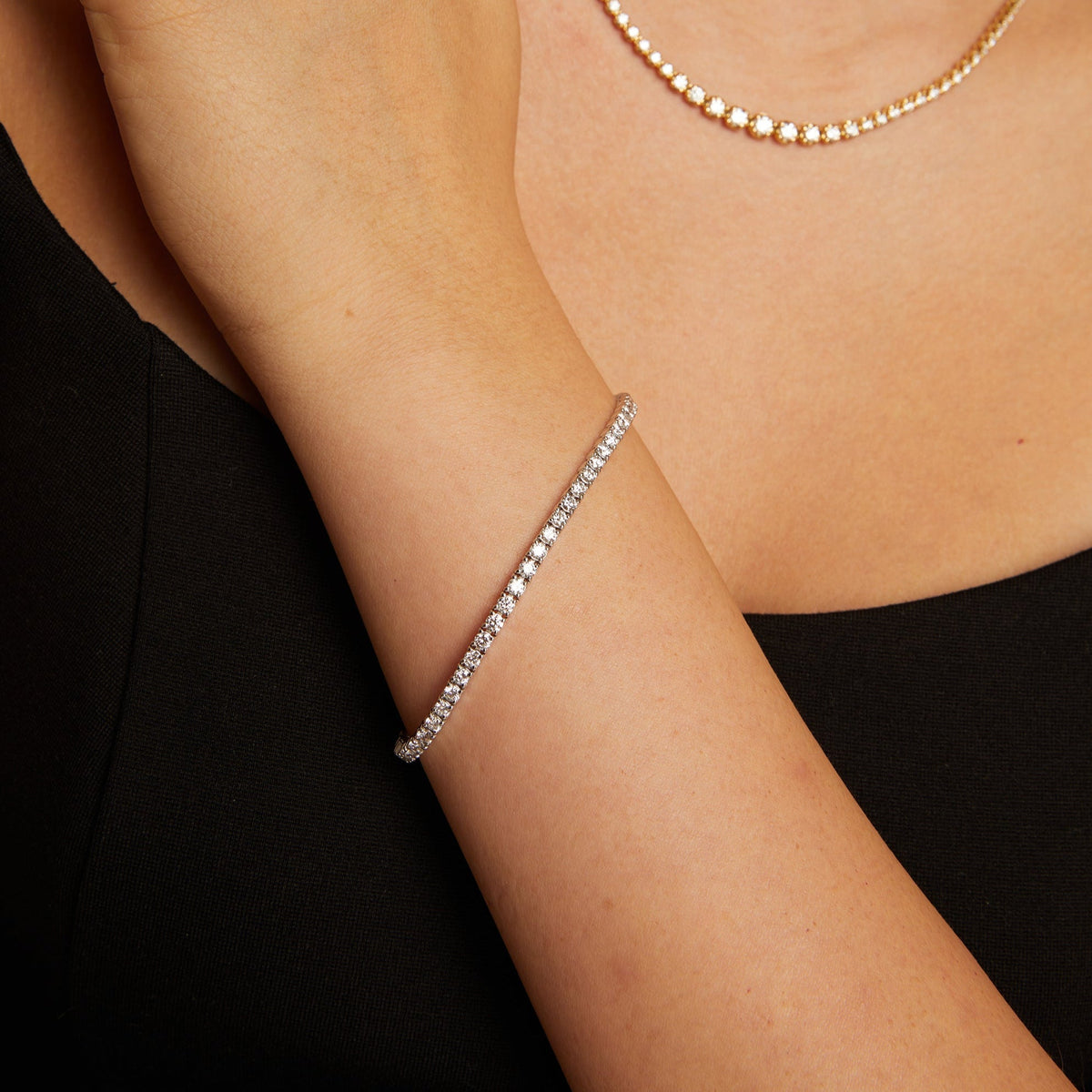 Model. Close-up of a person wearing a gold necklace, ring, and bracelet on a black background
