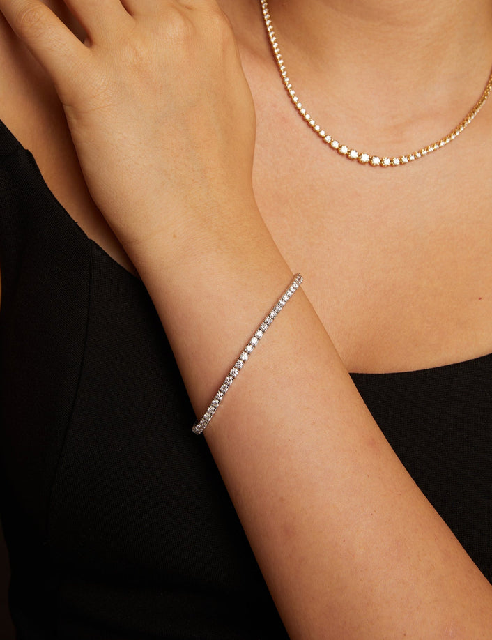 Model. Close-up of a person wearing a gold ring, necklace, and bracelet on a neutral background