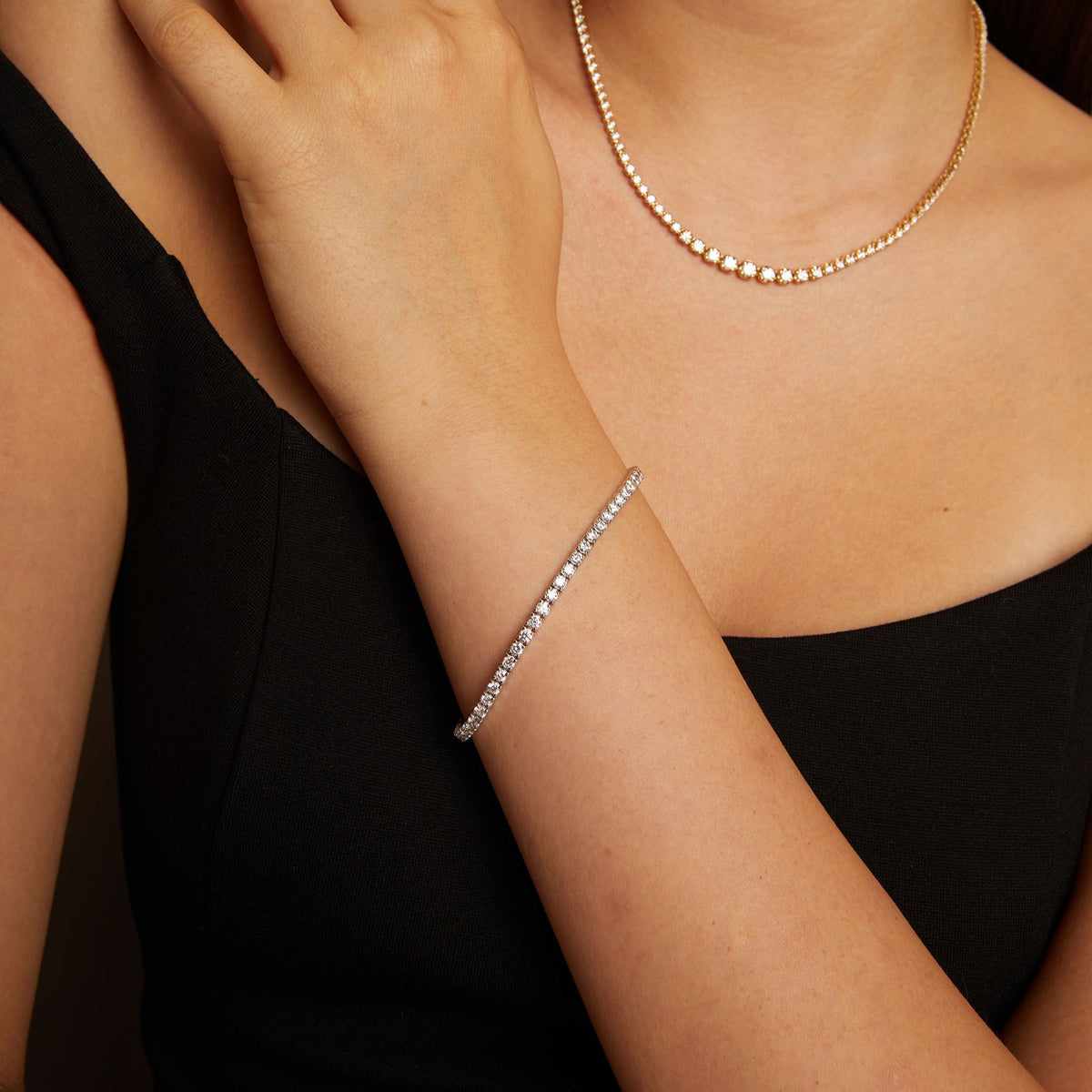Model. Close-up of a person wearing a gold ring, necklace, and bracelet on a neutral background