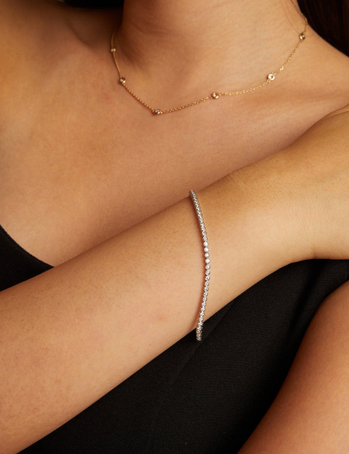Model. Close-up of a woman wearing a gold necklace and bracelet against a neutral background