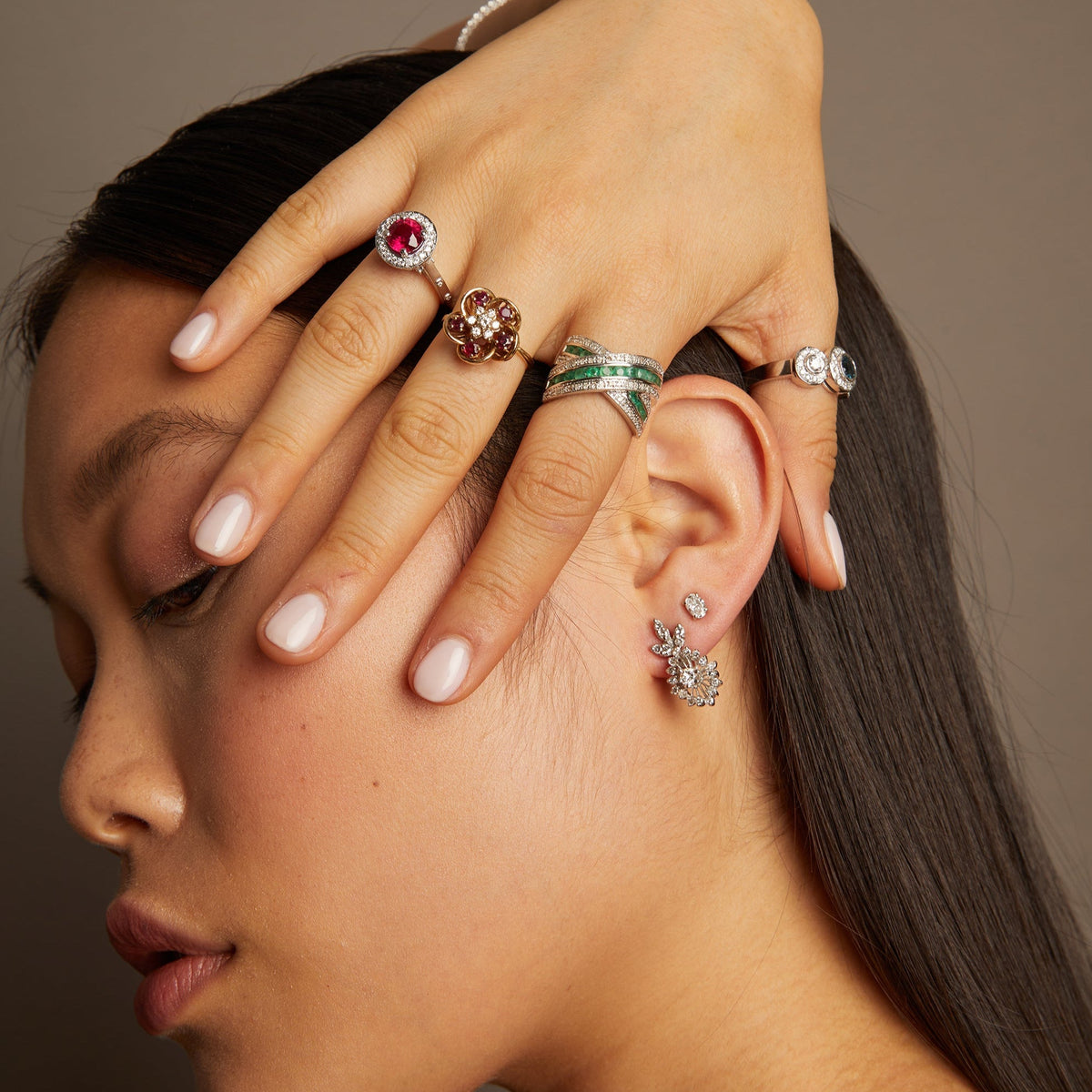 Model. Close-up of a woman's face with jewelry on her hand and ear against a neutral background