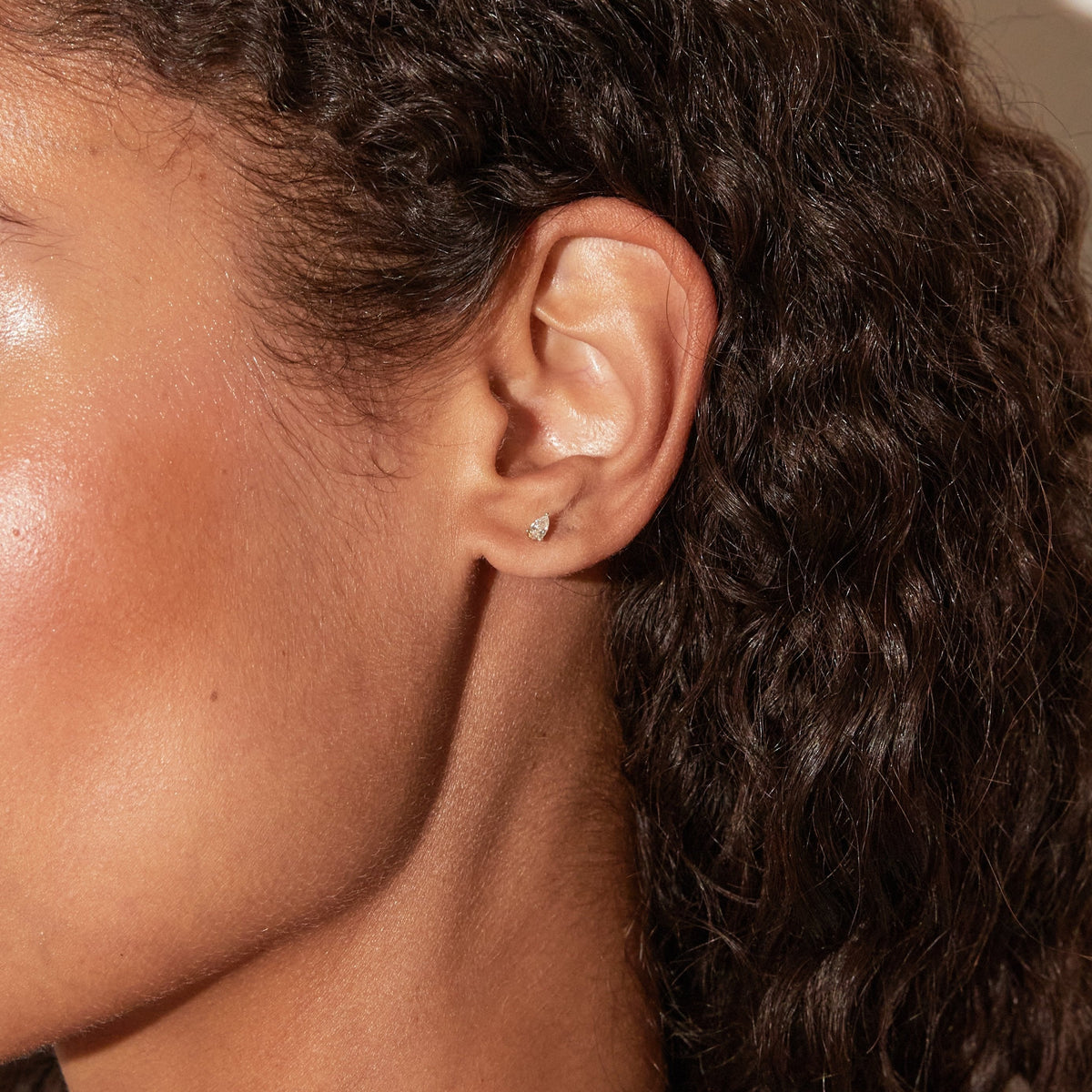 Model. Close-up of an ear with dark hair and a small earring.