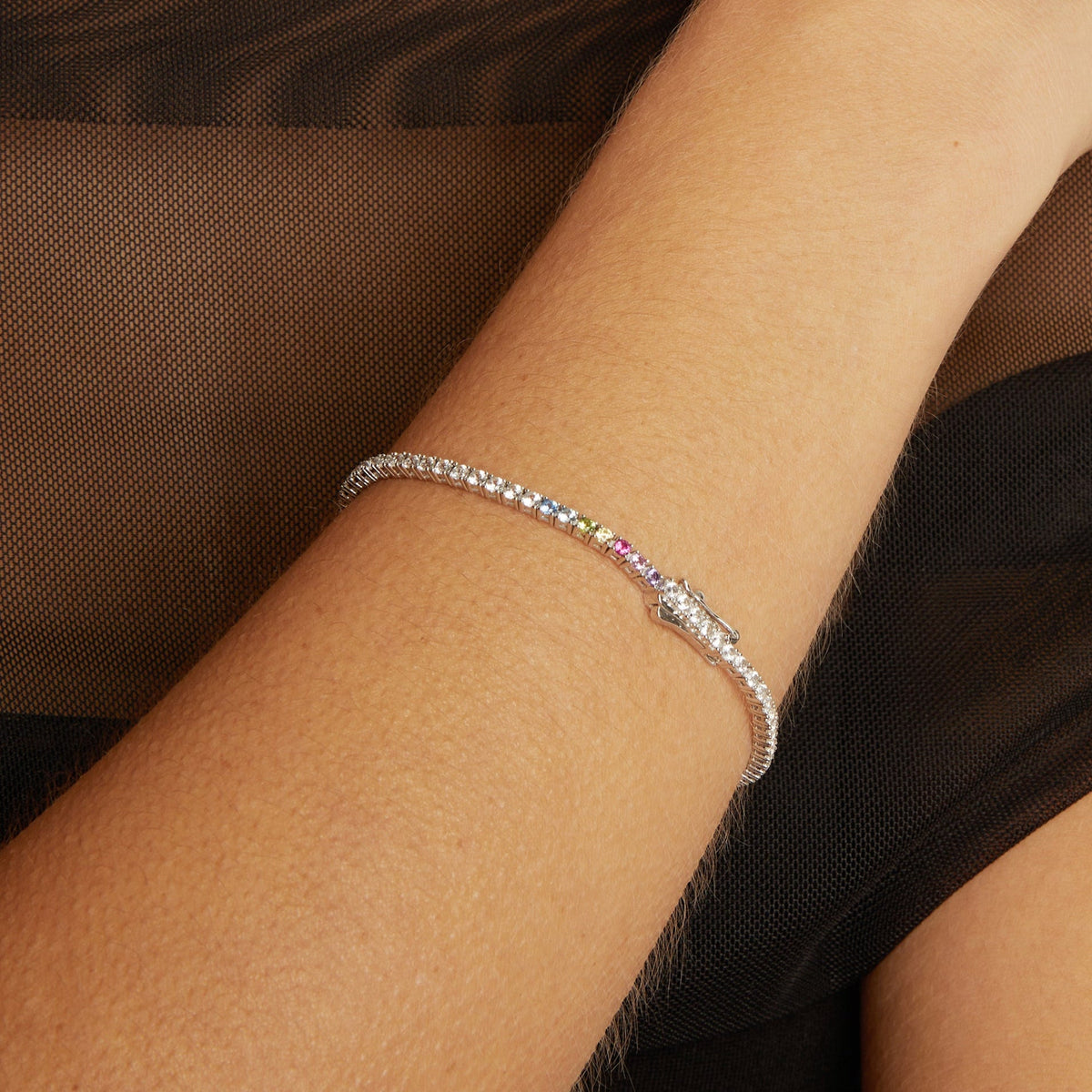 Model. Close-up of a wrist wearing a colorful bracelet against a brown background