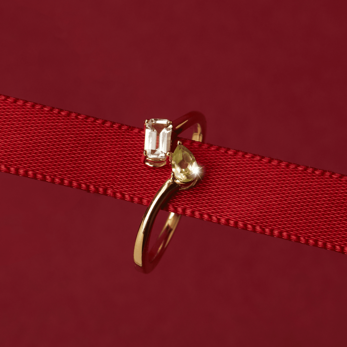 Flatlay Model Close-up of a gold two-stone ring with a clear and a yellow gemstone resting on a red ribbon.