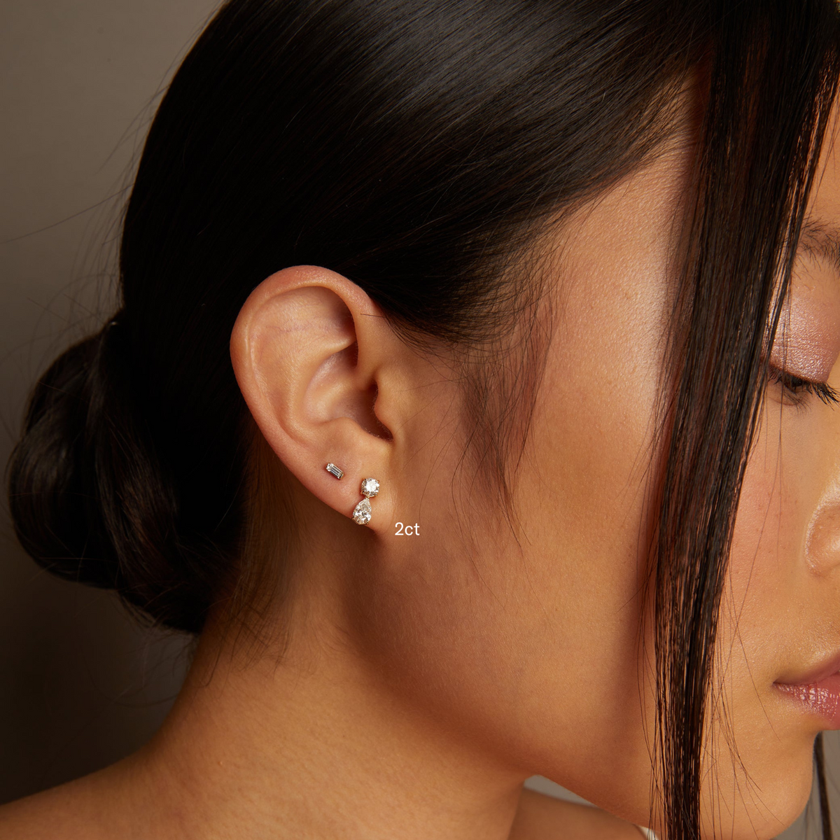 Model. Close-up of a woman's ear wearing diamond earrings with '2ct' label.