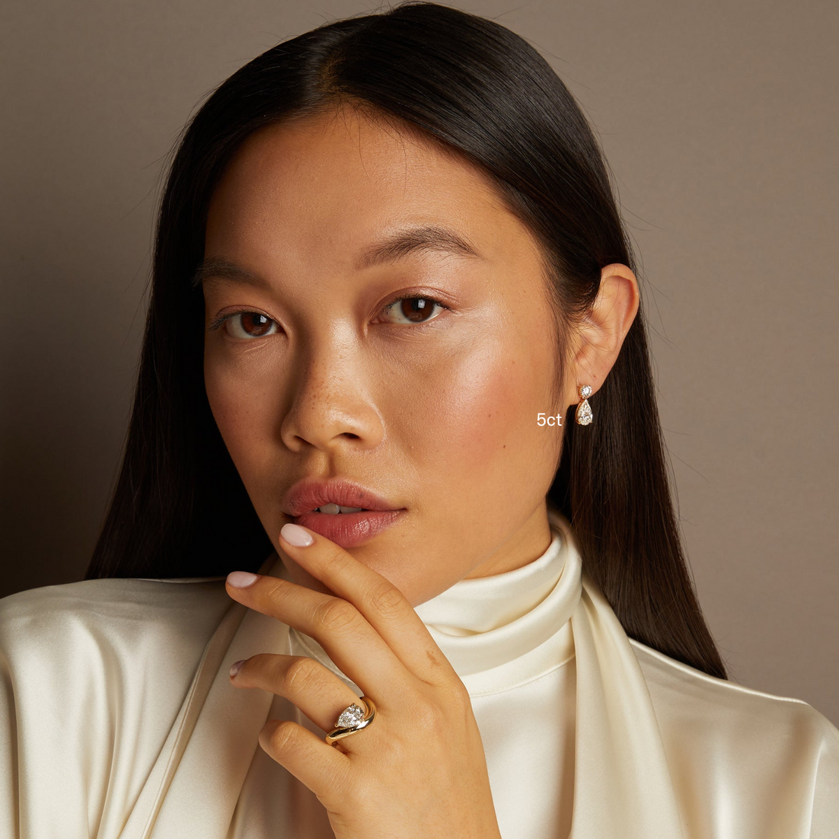 Model. Woman wearing a white turtleneck and diamond jewelry against a neutral background
