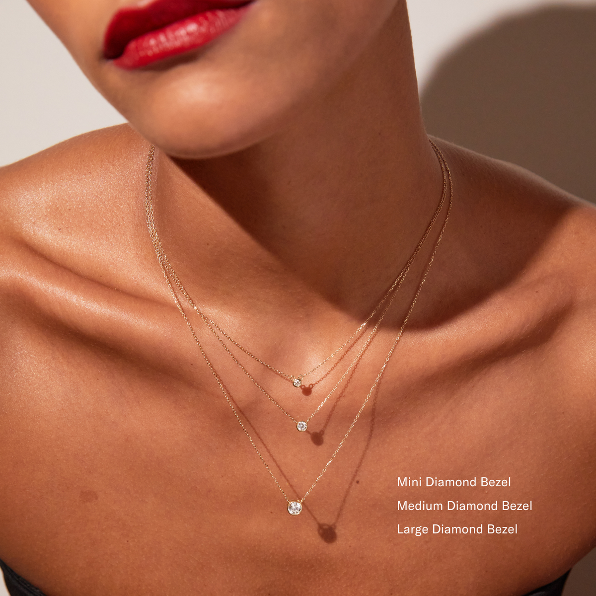 Model. Close up of woman wearing three diamond bezel necklace on a white background