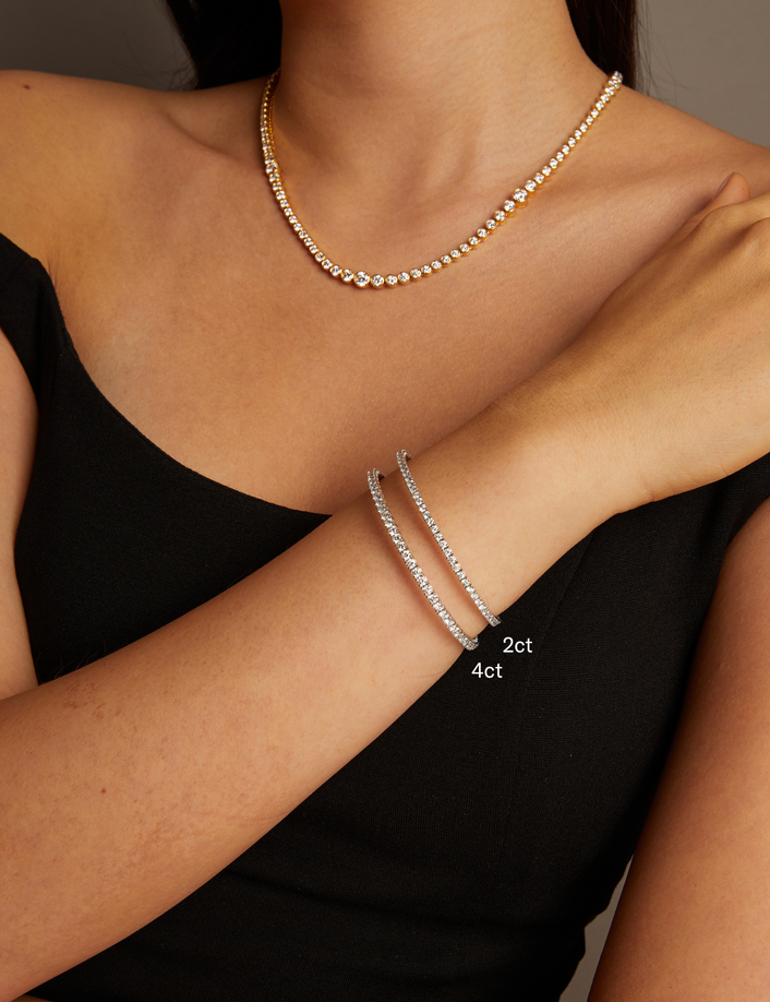 Model. Close-up of a person wearing a necklace and two silver bracelets on a neutral background