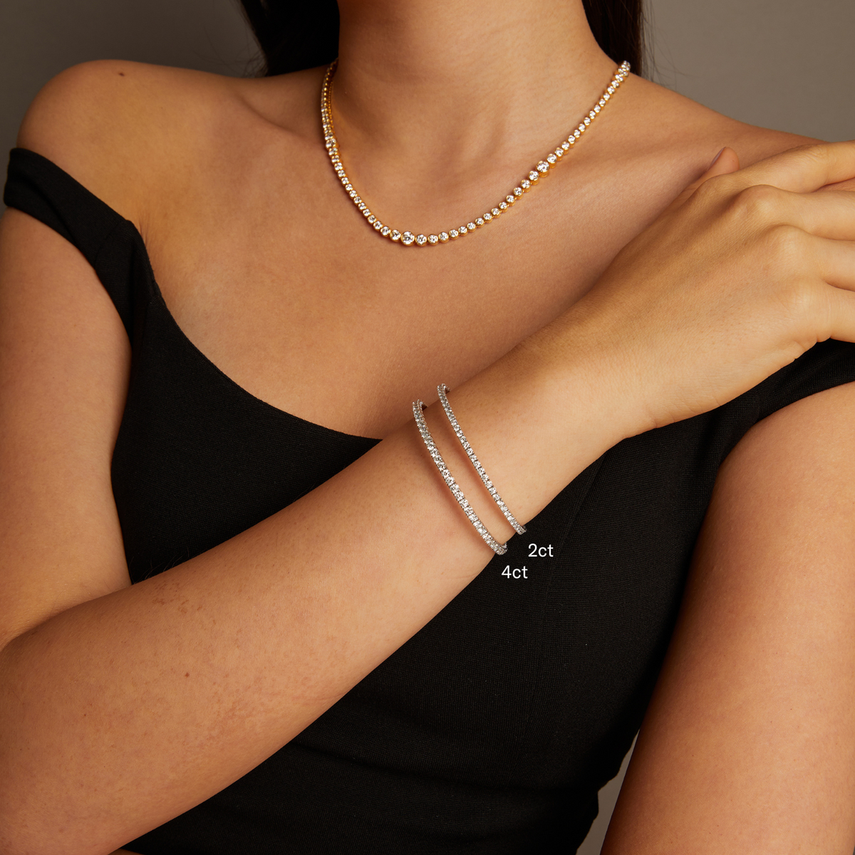Model. Close-up of a person wearing a necklace and two silver bracelets on a neutral background