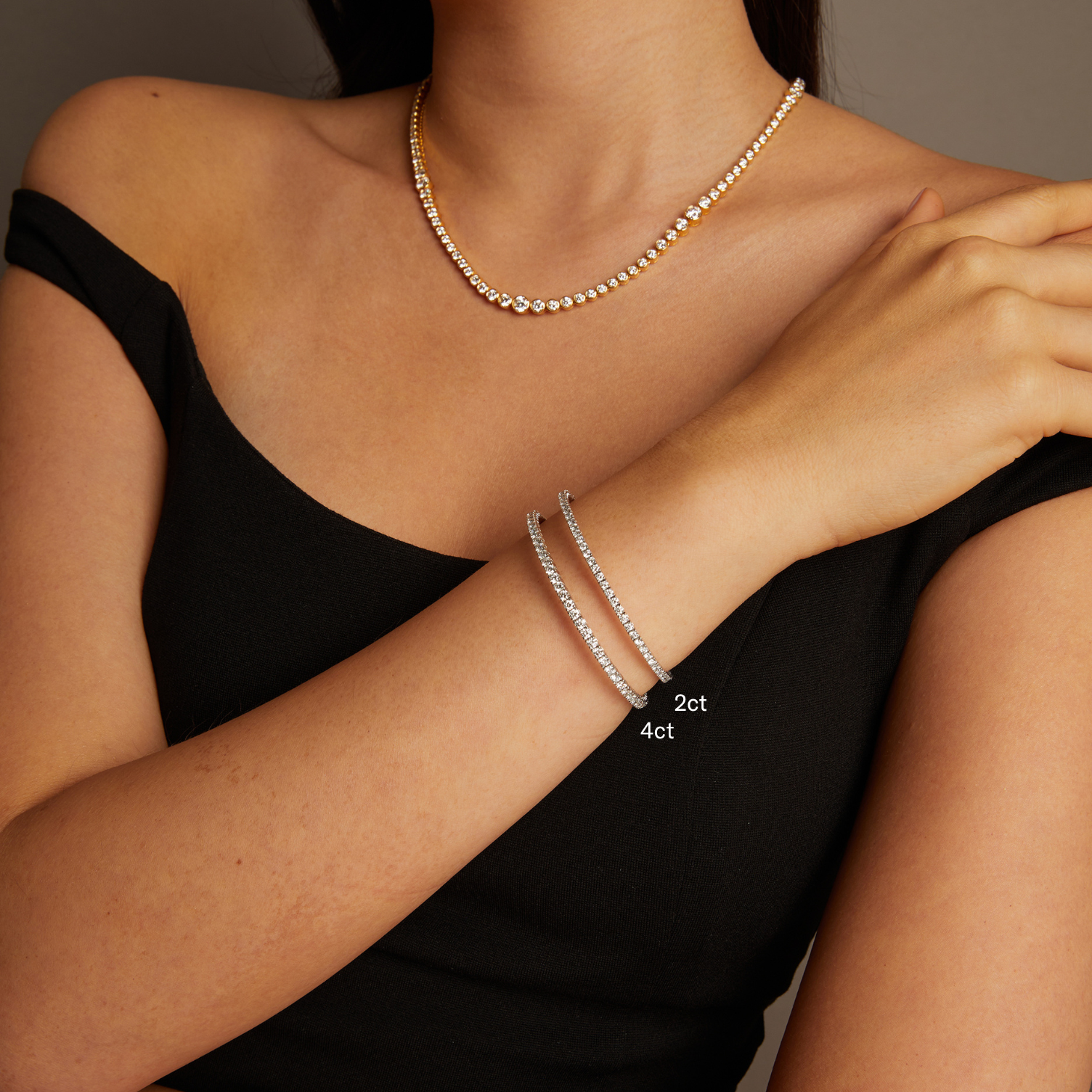 Model. Close-up of a person wearing a necklace and two silver bracelets on a neutral background