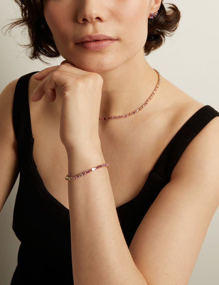 Woman wearing a pink tennis necklace and bracelet with a neutral background