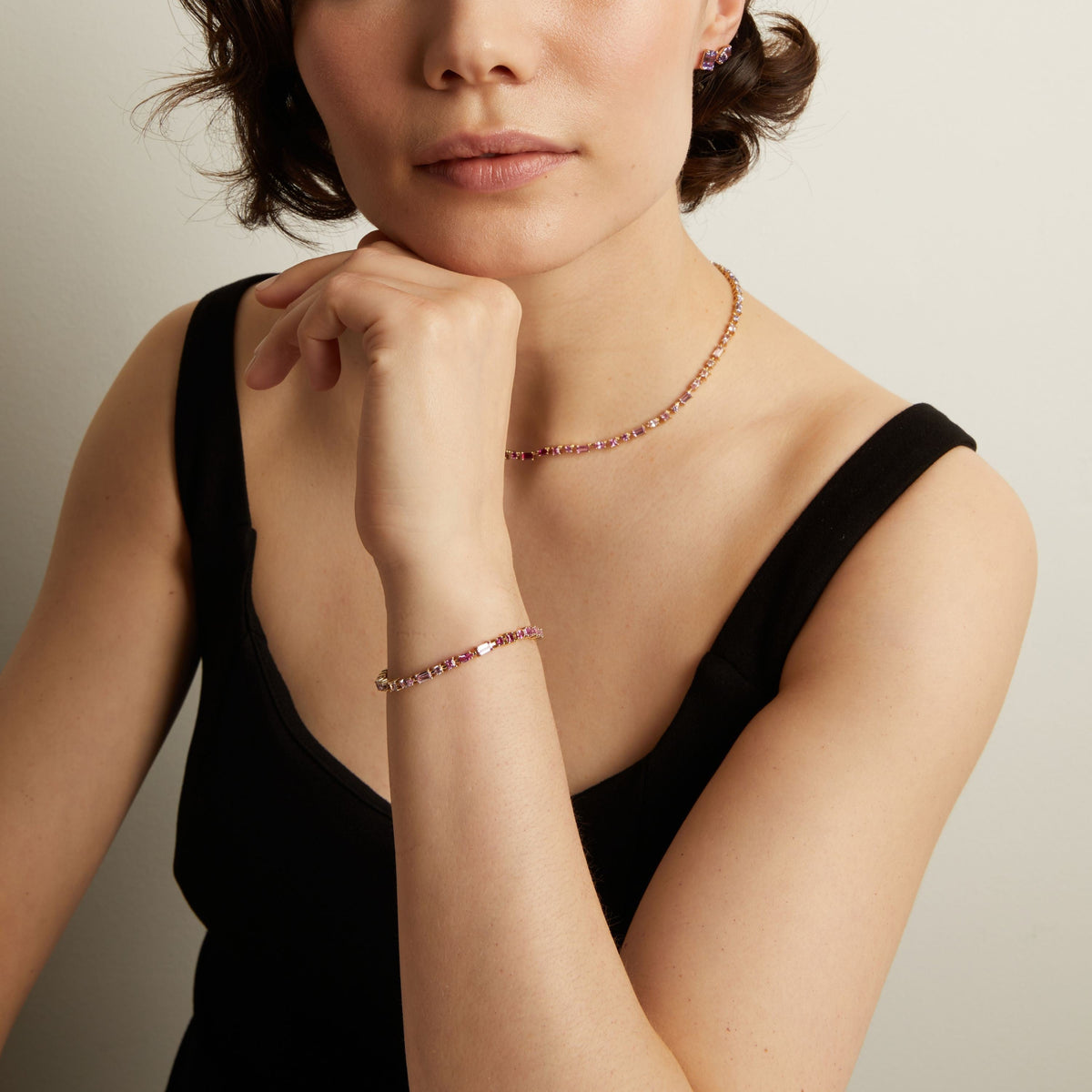 Woman wearing a pink tennis necklace and bracelet with a neutral background