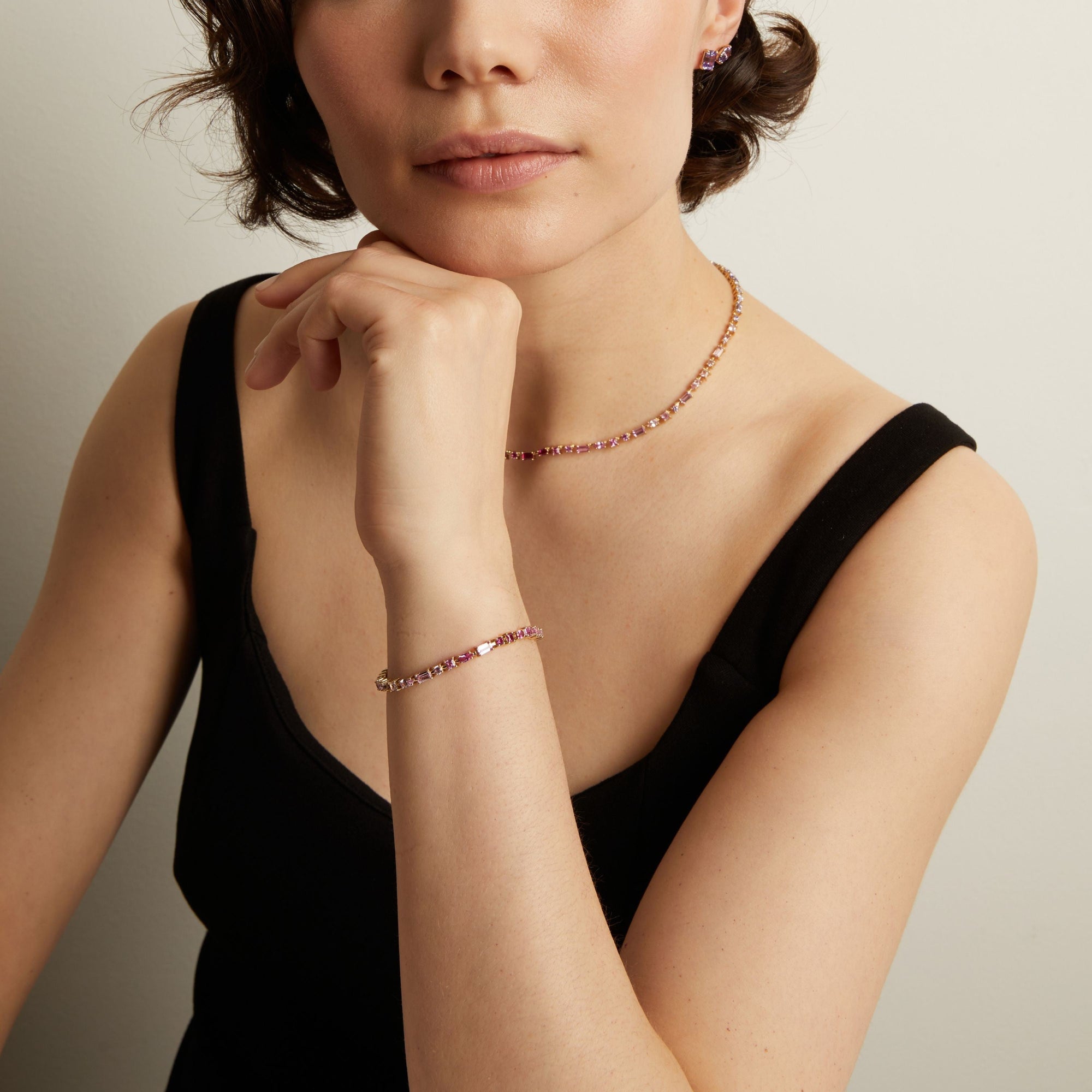 Woman wearing a pink tennis necklace and bracelet with a neutral background