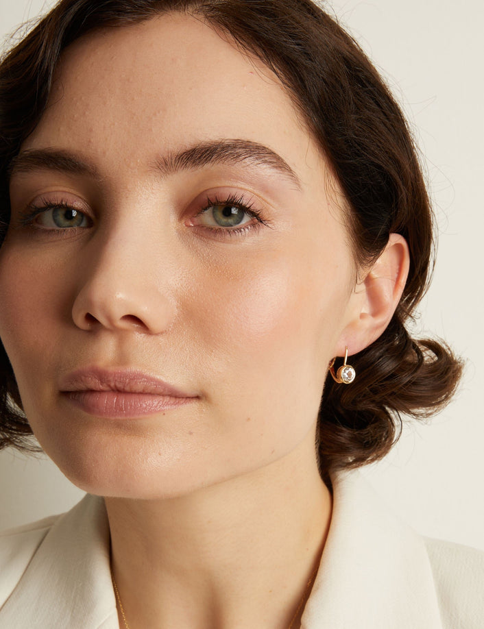 Model. Close-up of a woman wearing gemstone hoop earrings with a neutral background