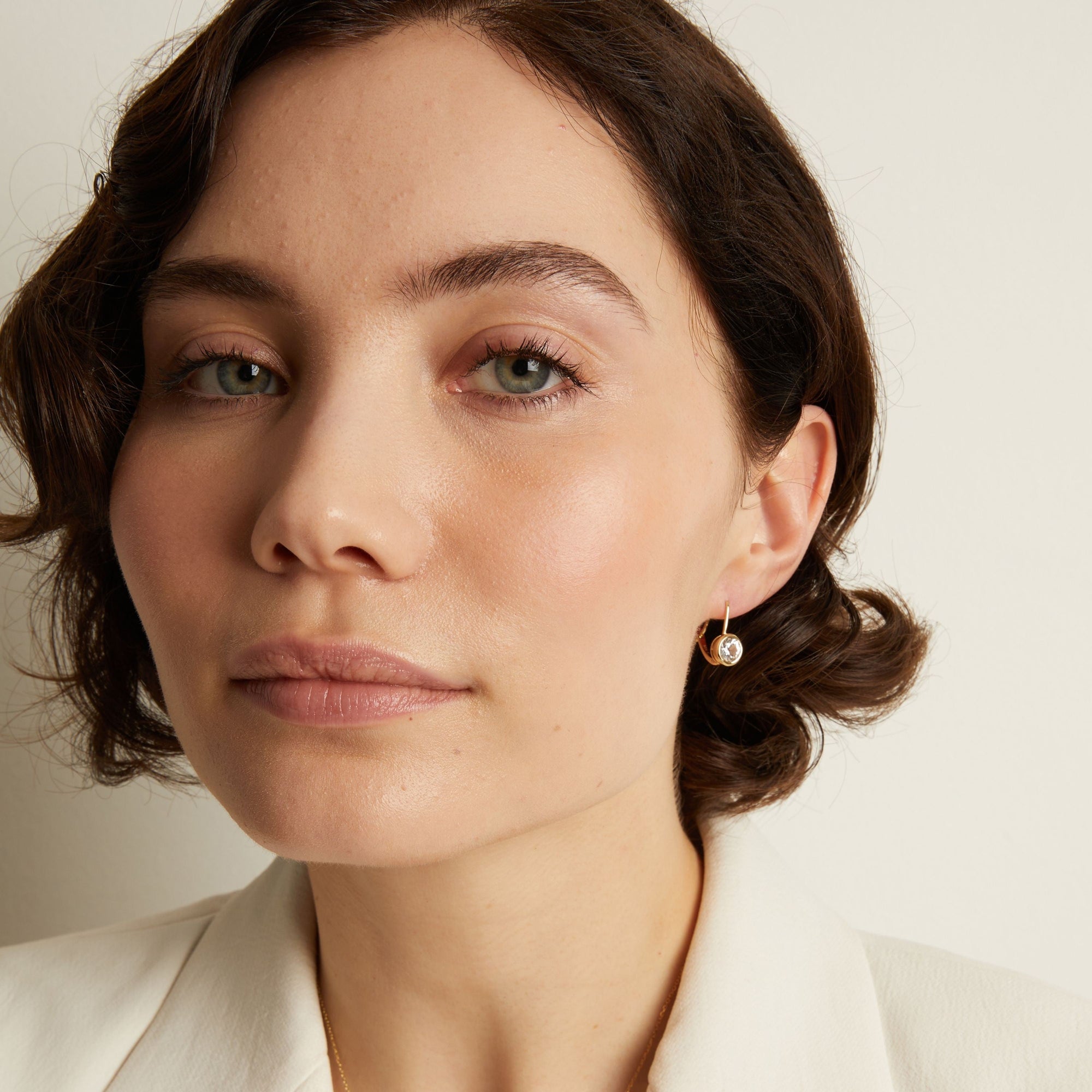 Model. Close-up of a woman wearing gemstone hoop earrings with a neutral background