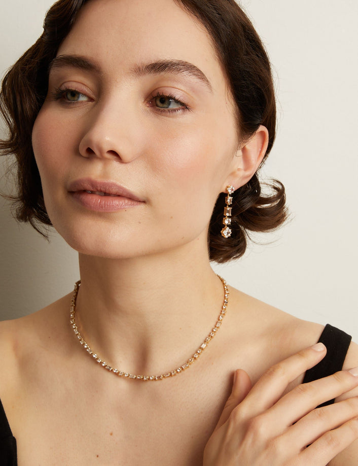 Model. Woman wearing a tennis necklace and earrings against a neutral background