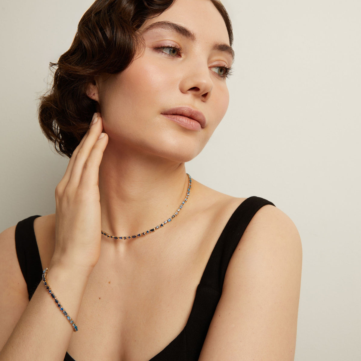 Woman wearing a blue tennis necklace and bracelet on a plain background. Model