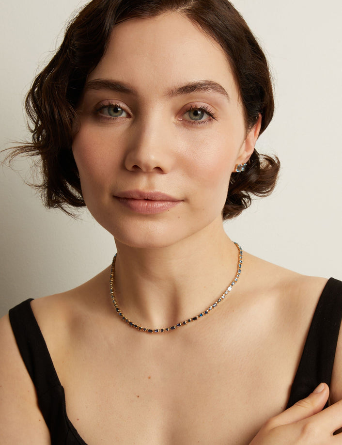 Woman wearing a blue tennis necklace against a neutral background. Model