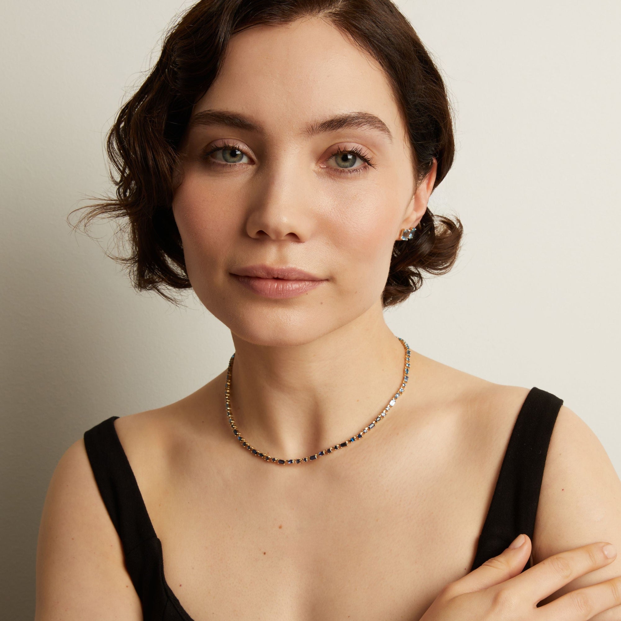 Woman wearing a blue tennis necklace against a neutral background. Model