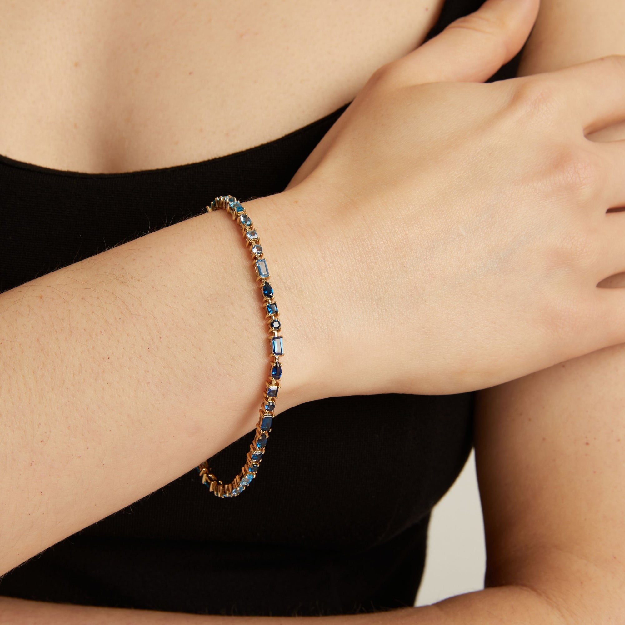 Close-up of a person's wrist wearing a blue tennis bracelet on a neutral background. 